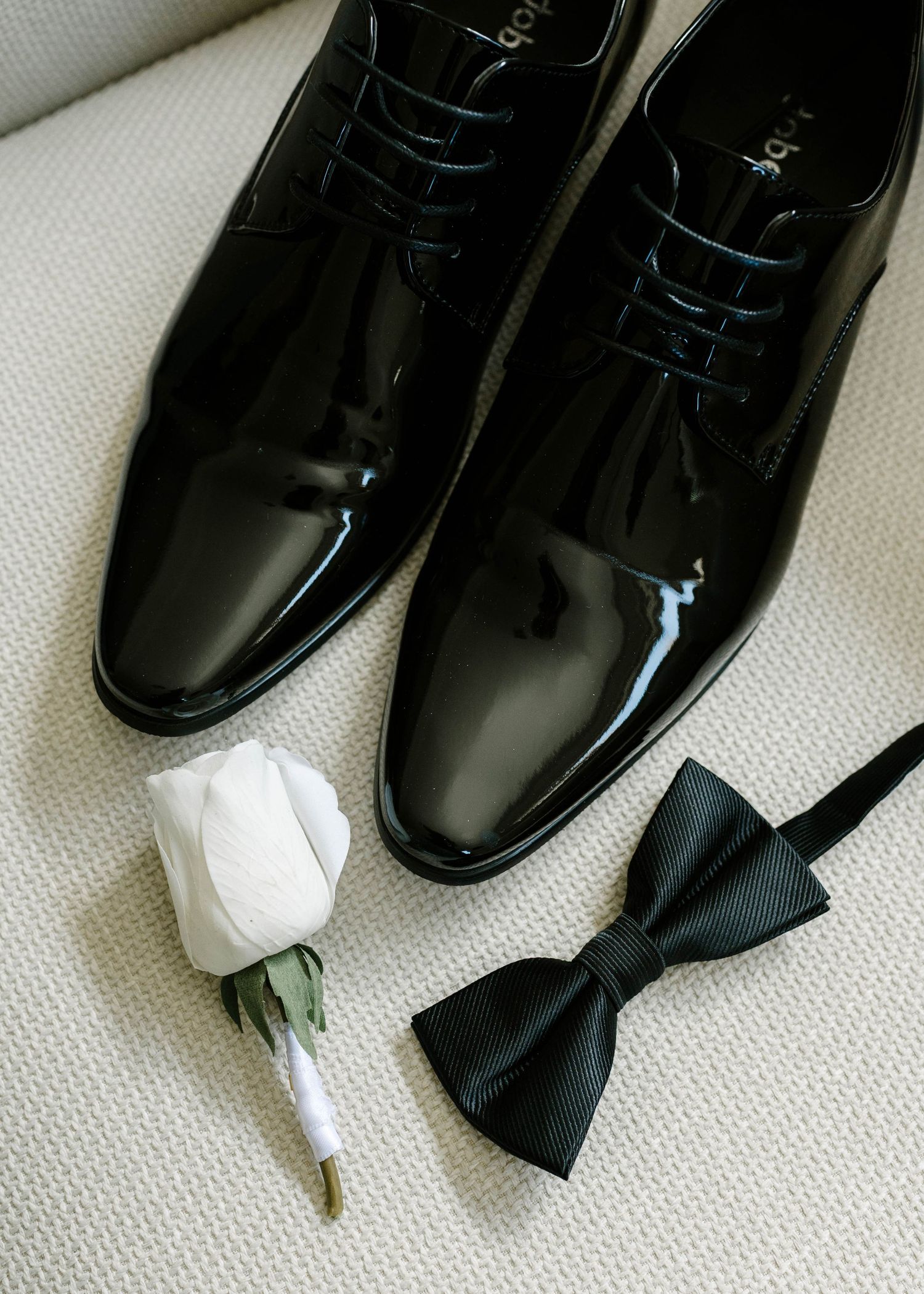 A series of five black leather dress shoes being polished and shined on a white textured surface.