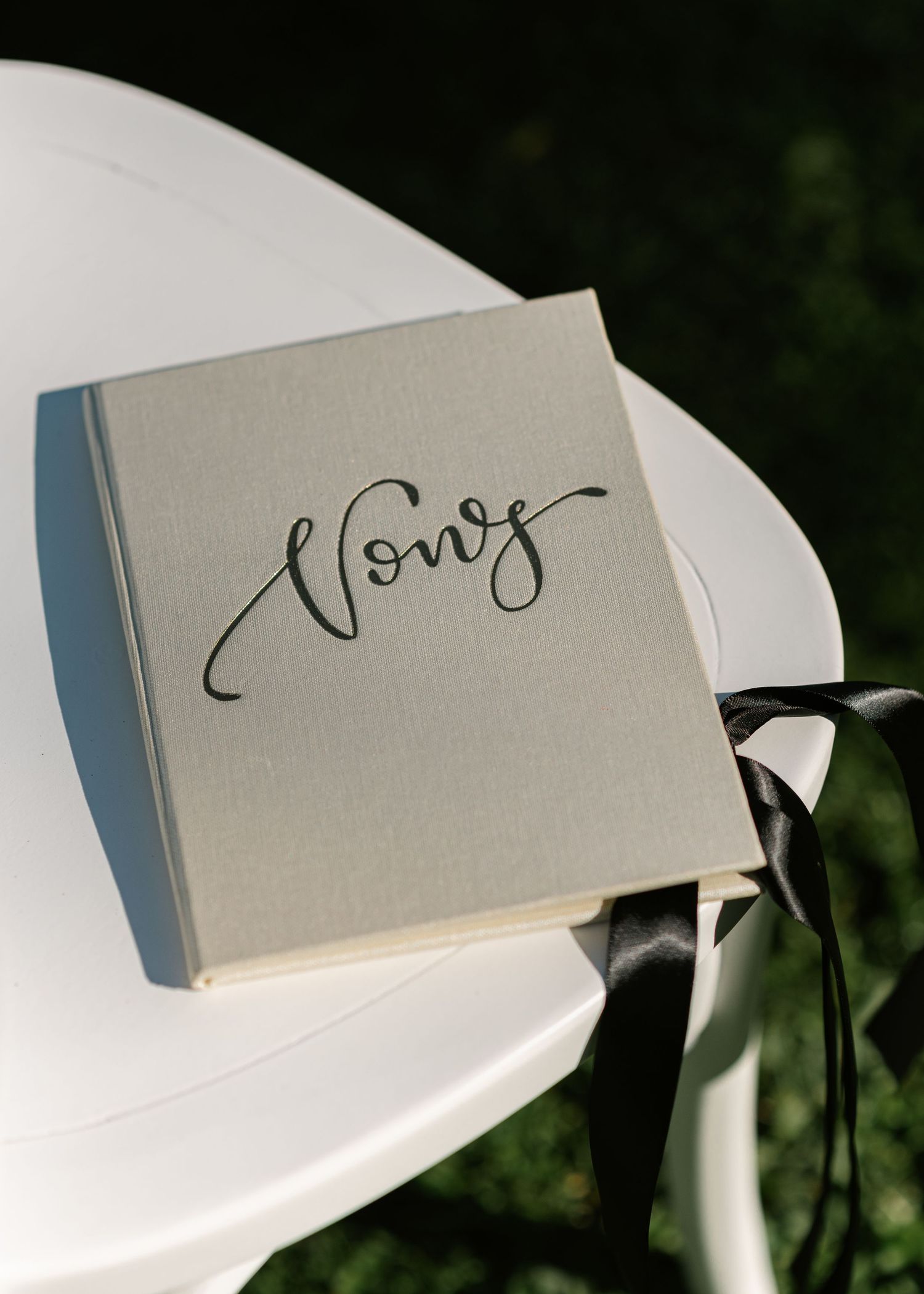 Elegant gray linen vows book with black ribbon and calligraphy script, resting on a white table at a wedding ceremony.