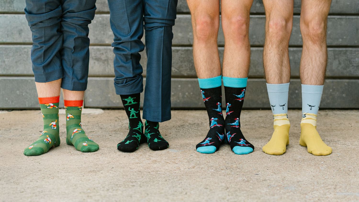 Four people wearing colorful novelty socks with fun patterns including dinosaurs and birds, showcasing playful sock designs.