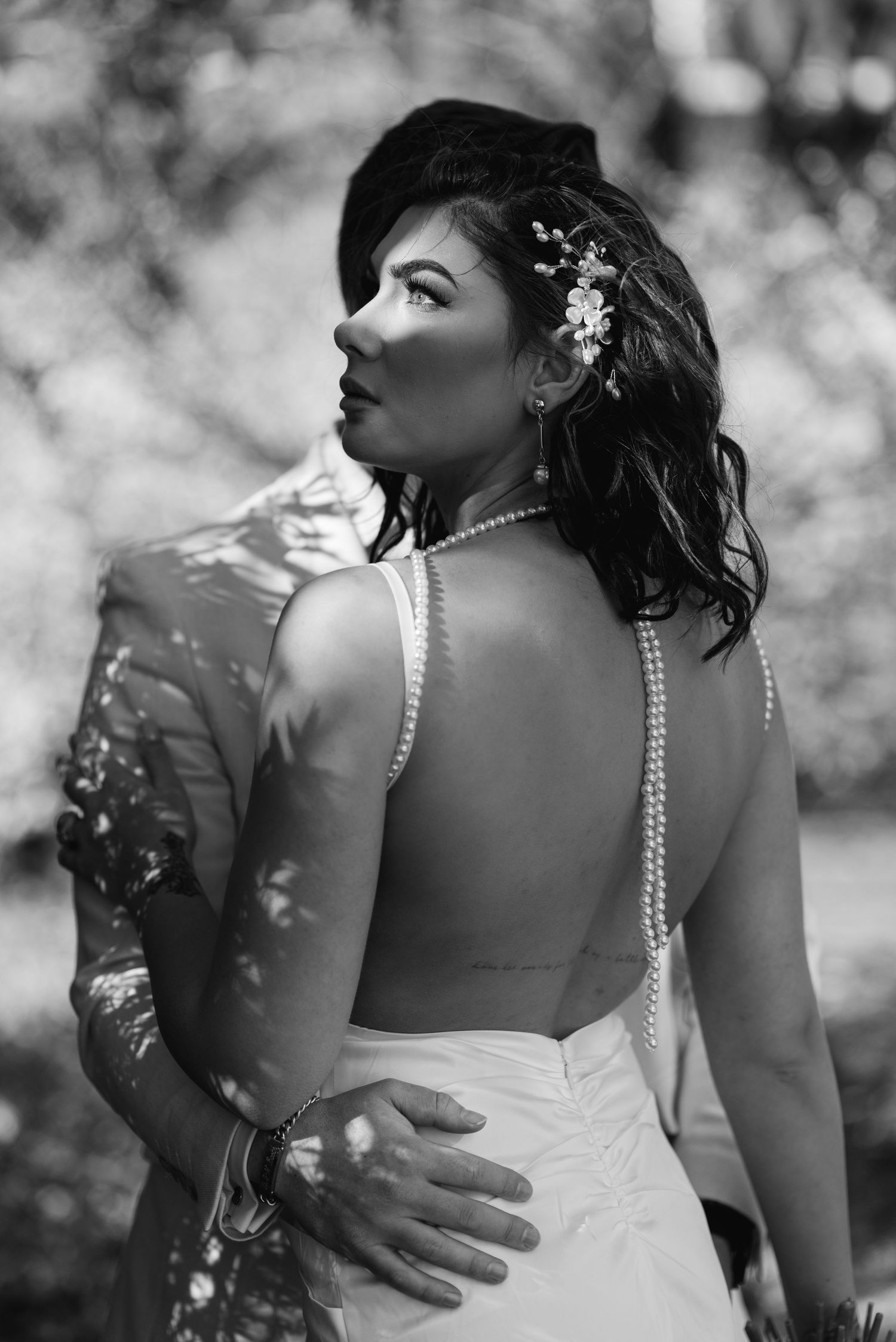 A series of black and white wedding photos showing a bride in a strapless gown with pearl details from behind.
