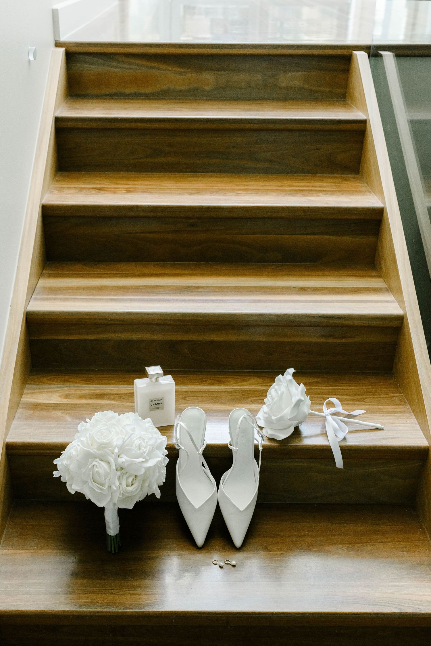 White bridal heels, rose bouquet, and accessories arranged on wooden staircase steps for a wedding day flat lay.