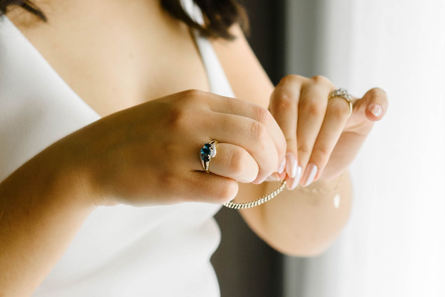 Close-up view of hands applying white nail polish to fingernails against a blurred neutral background.