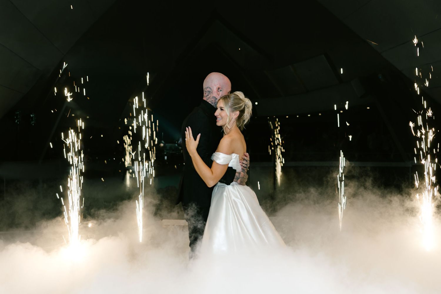 Bride and groom share first dance surrounded by sparkling pyrotechnics and dramatic fog at elegant wedding reception.