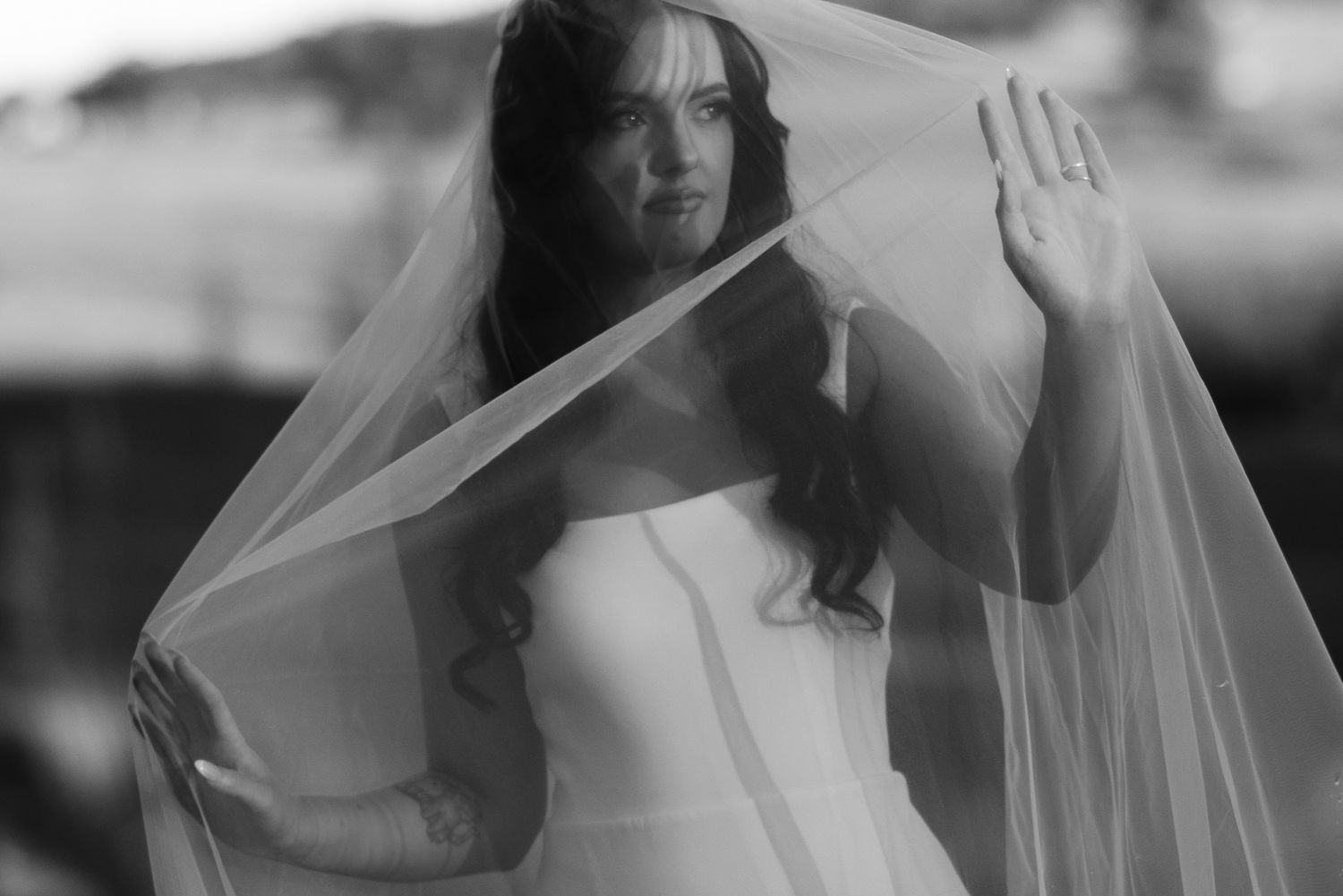 Black and white photo of a bride in a white gown lifting her veil gracefully on her wedding day.
