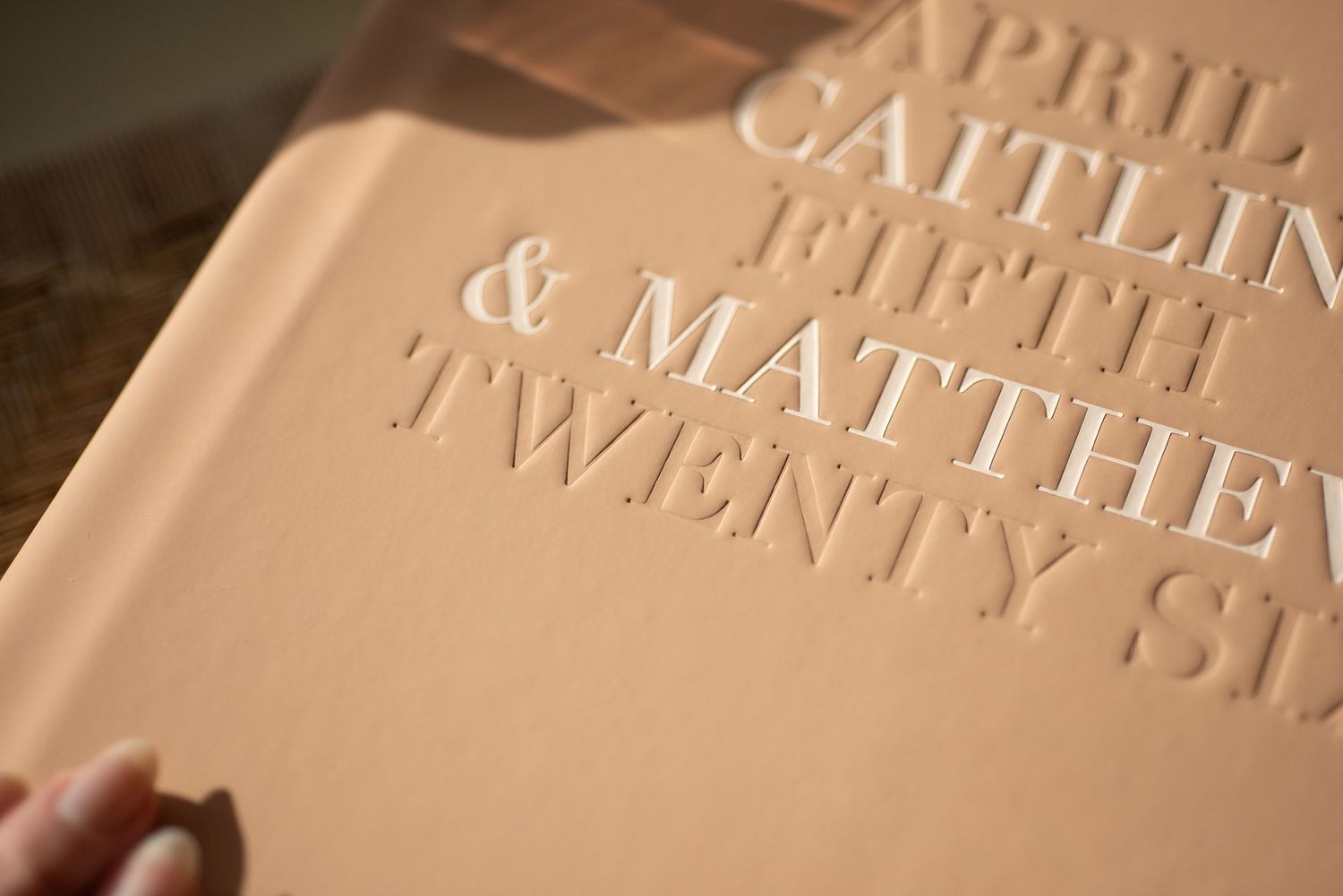 Close-up of an embossed tan hardcover wedding guest book with elegant serif text for Caitlin and Matthew.