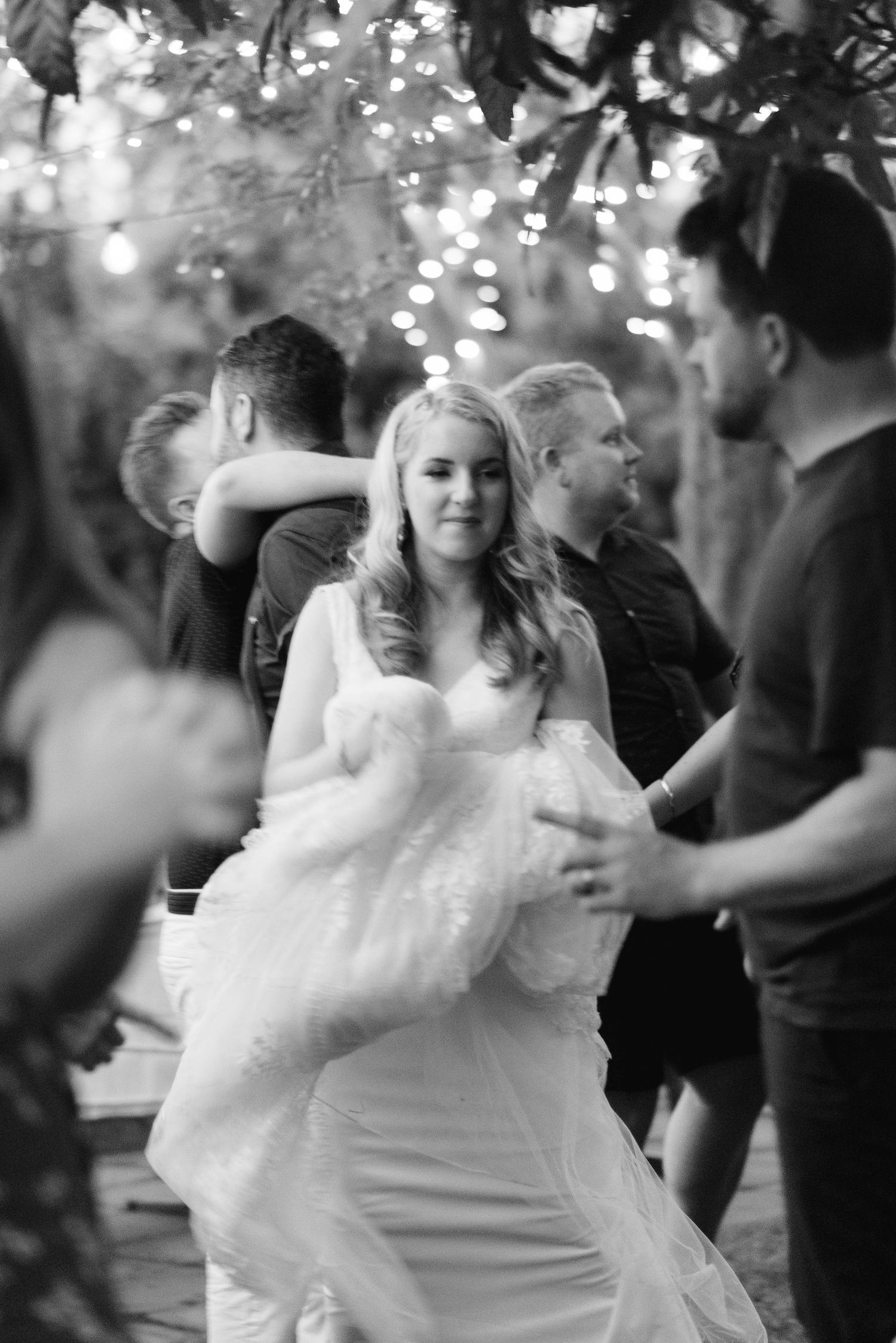 A bride in a white dress dances joyfully at an outdoor wedding reception.
