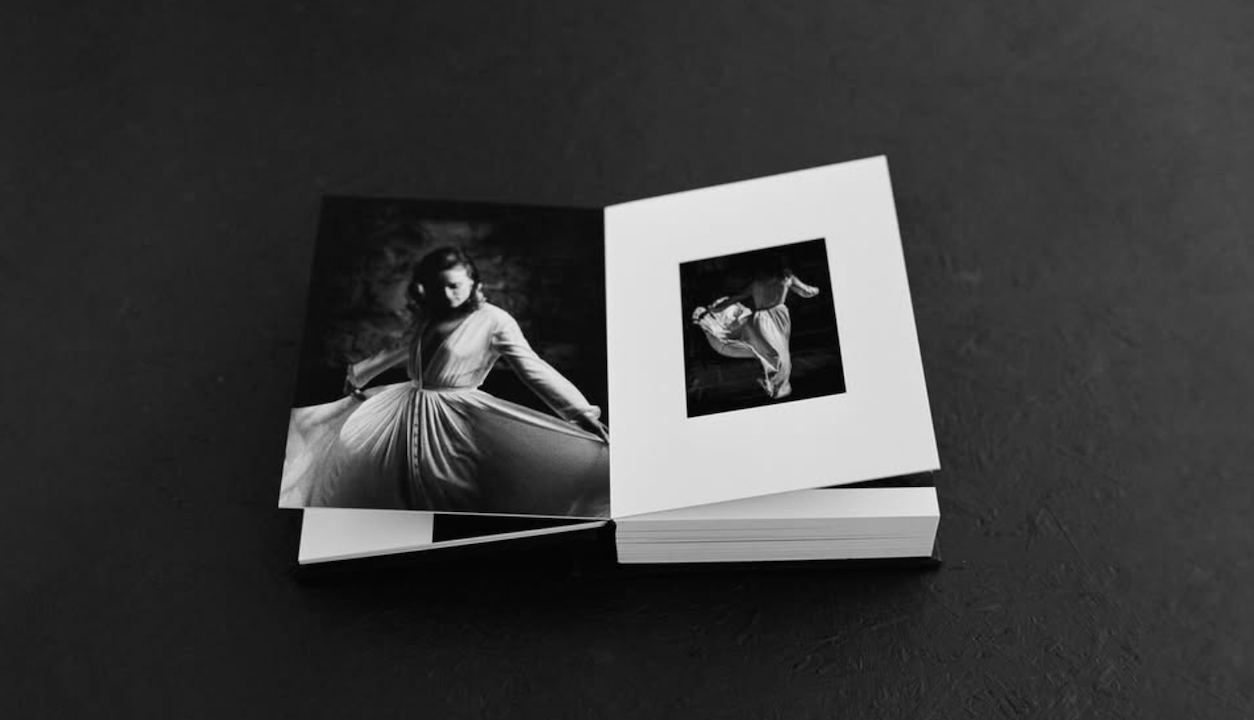 Black and white photo book open to elegant dance portraits on dark background.