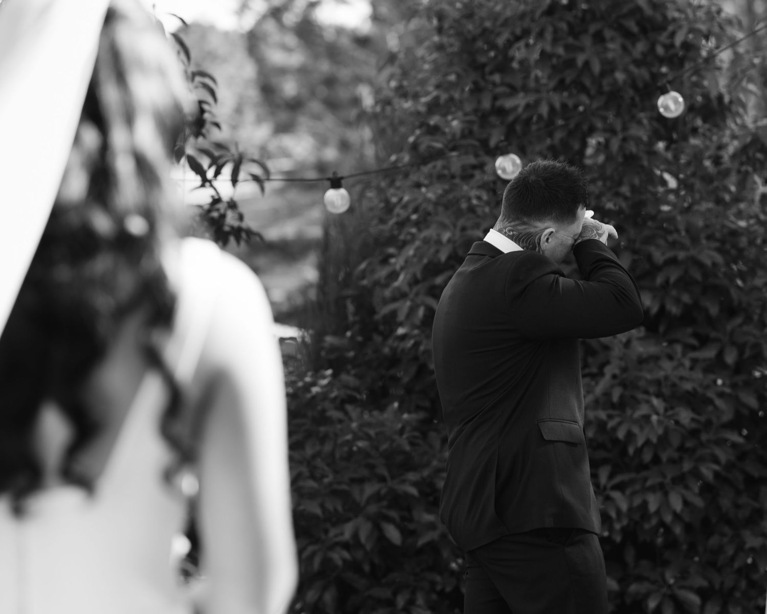 Emotional groom wiping tears during outdoor wedding ceremony in black and white photography.