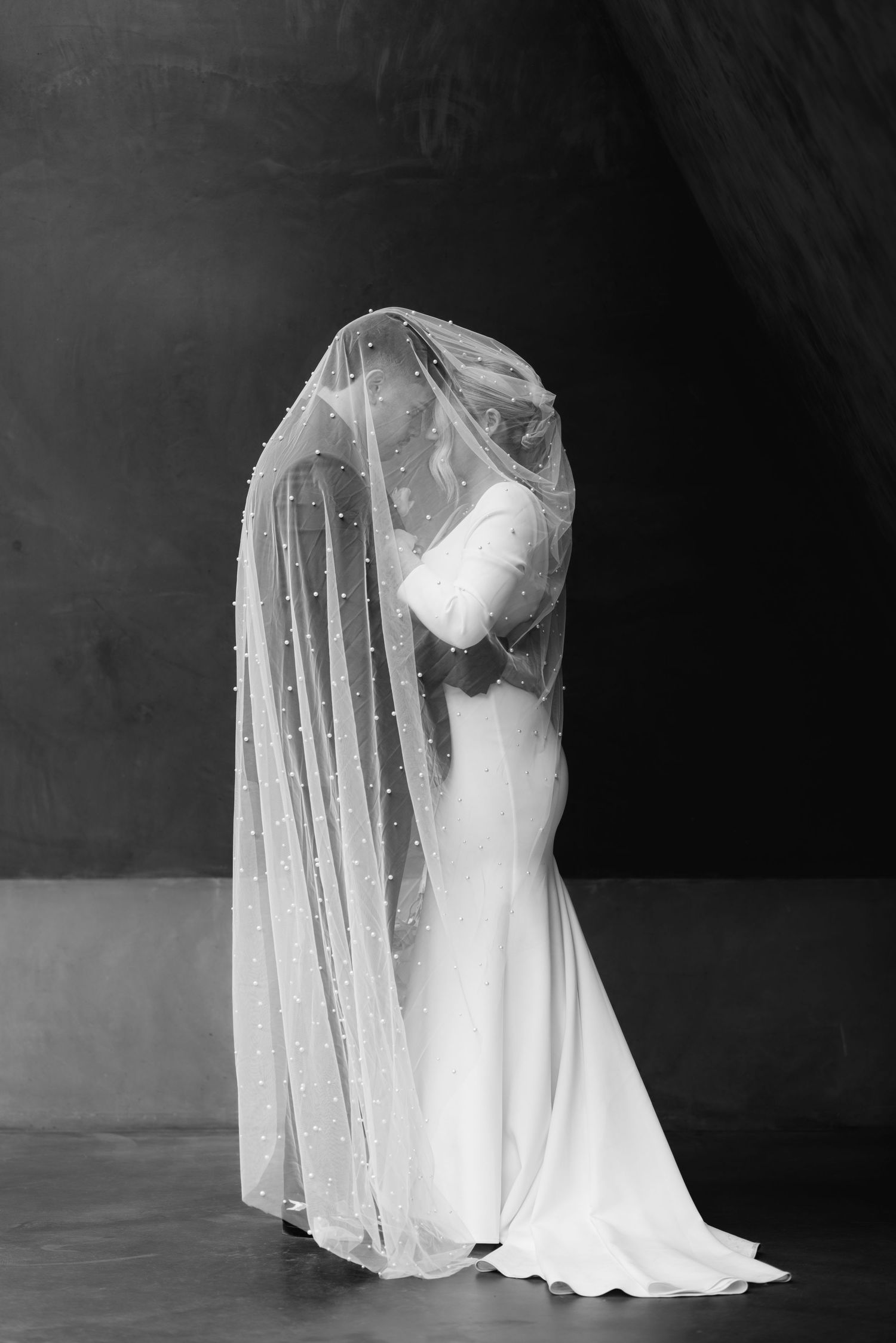 Elegant white wedding dress with flowing veil captured in dramatic black and white photography.