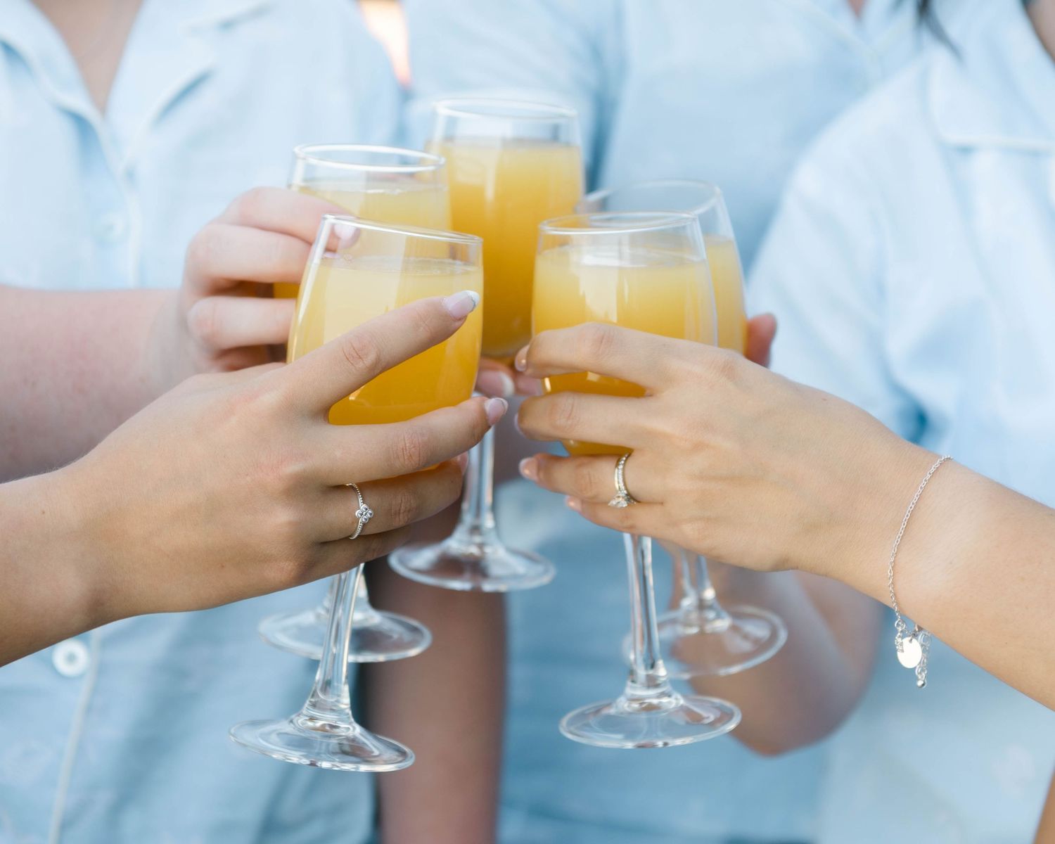 Friends in light blue attire toasting with mimosa cocktails in champagne glasses.
