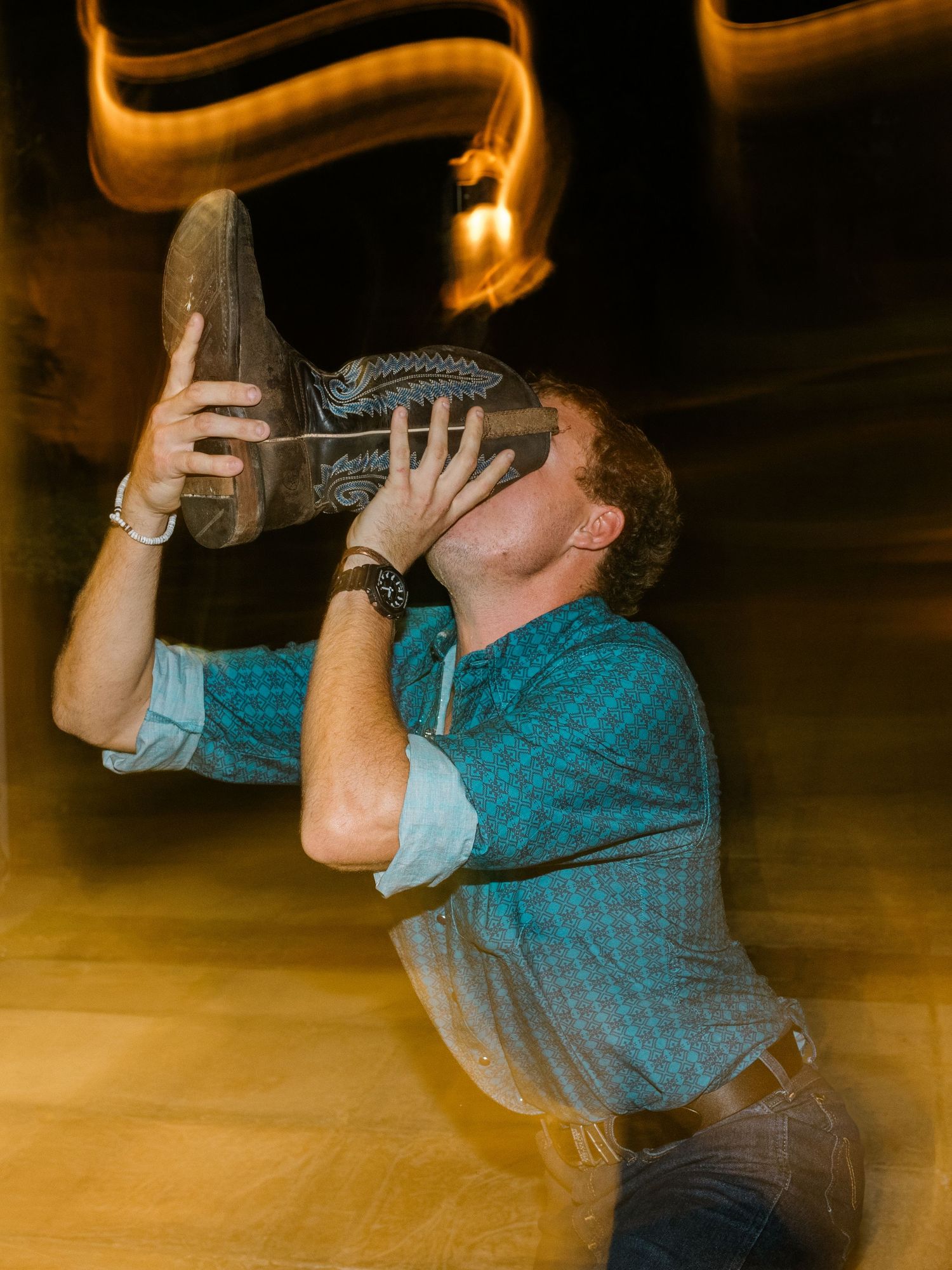 A person in a turquoise shirt drinks from a large wine bottle at an event.