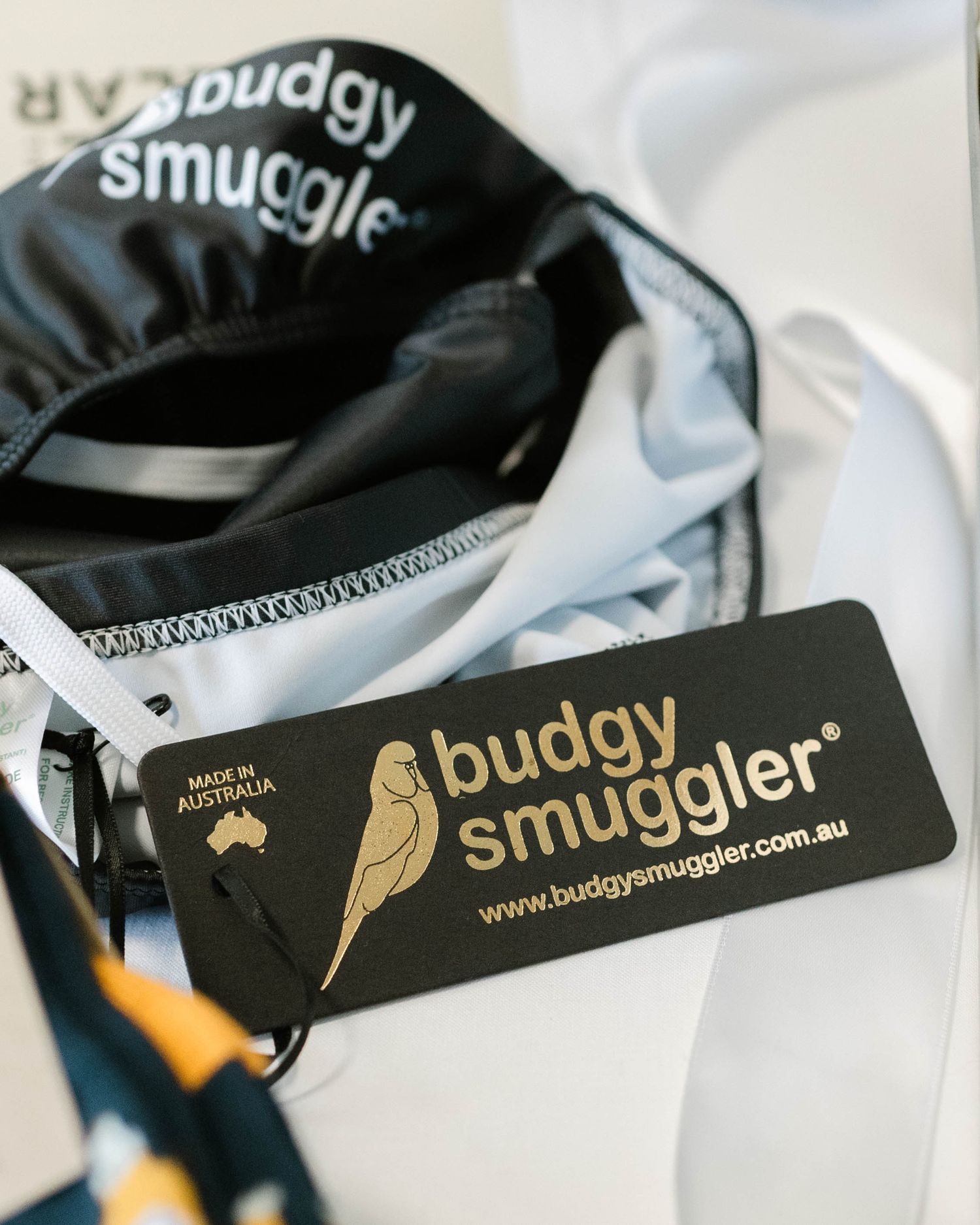 Close-up shot of a Budgy Smuggler brand tag and black swimwear fabric with stitching details.