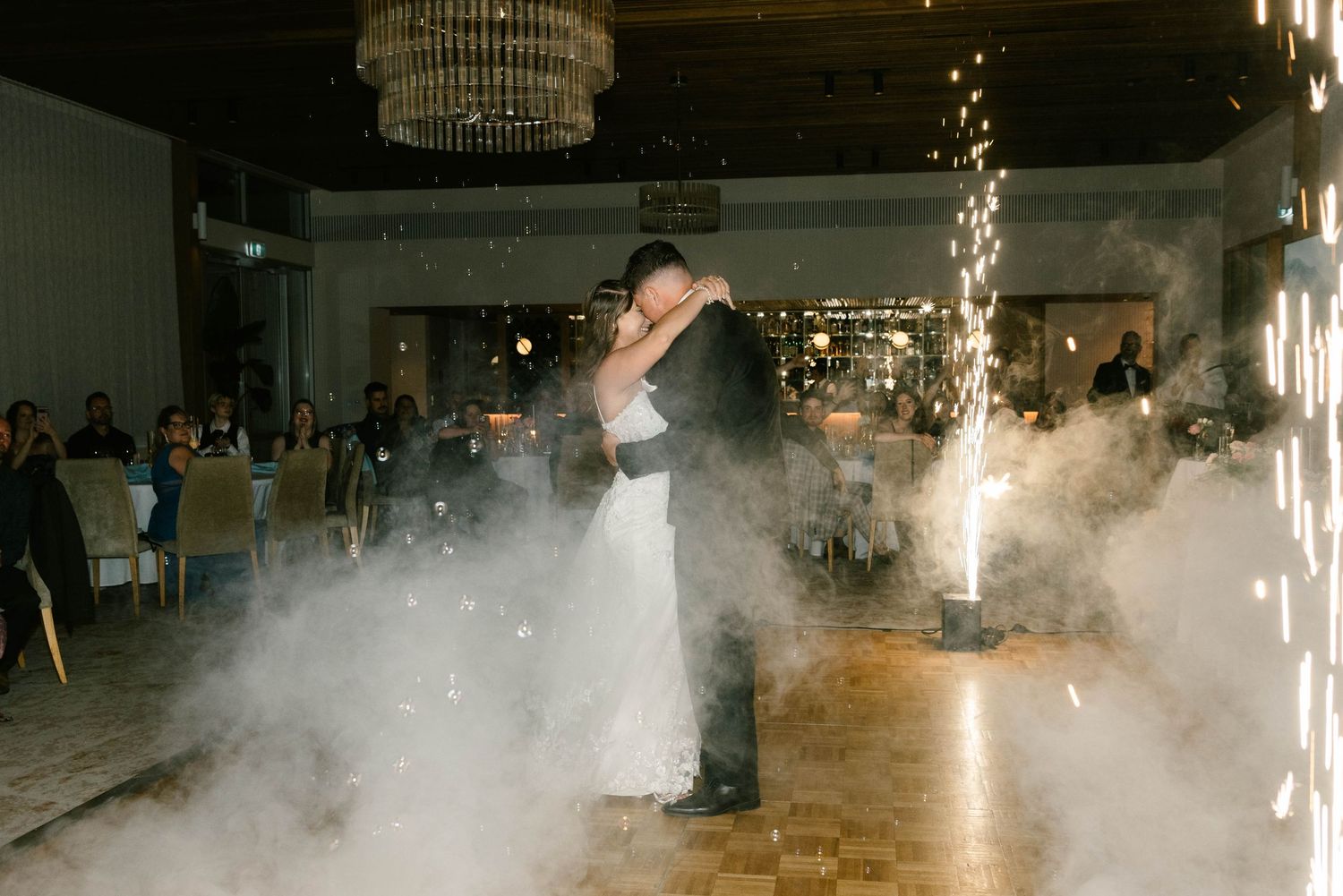 Fog machines create a dramatic atmosphere on a dance floor under elegant chandeliers at an indoor event.