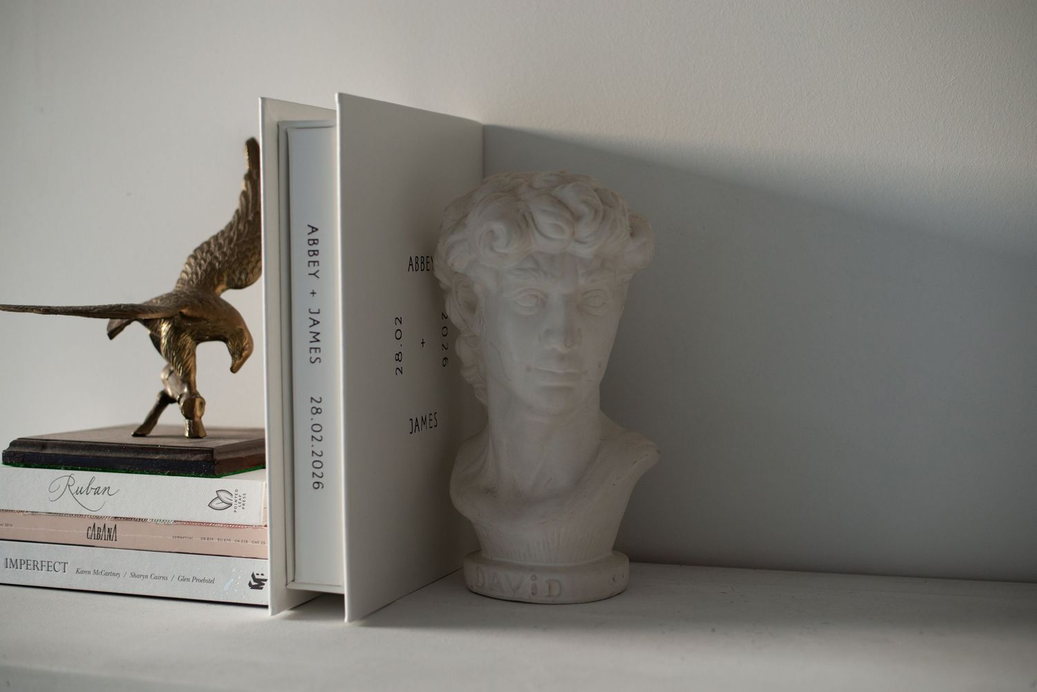 White shelf with gold dinosaur figurine, stacked books, and a marble David bust sculpture as bookends.