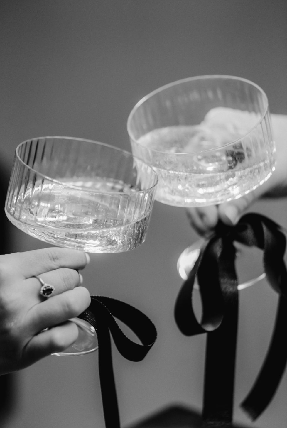 Black and white image of champagne glasses clinking together in a celebratory toast.