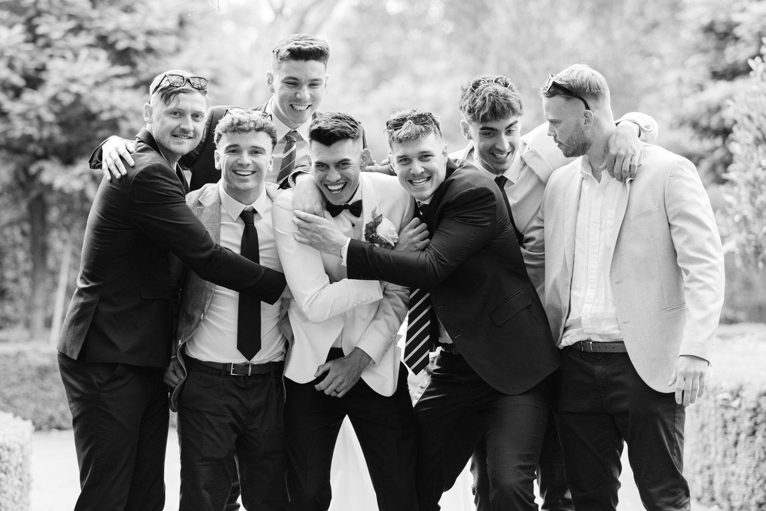 Groomsmen laughing together outdoors during wedding photo session.