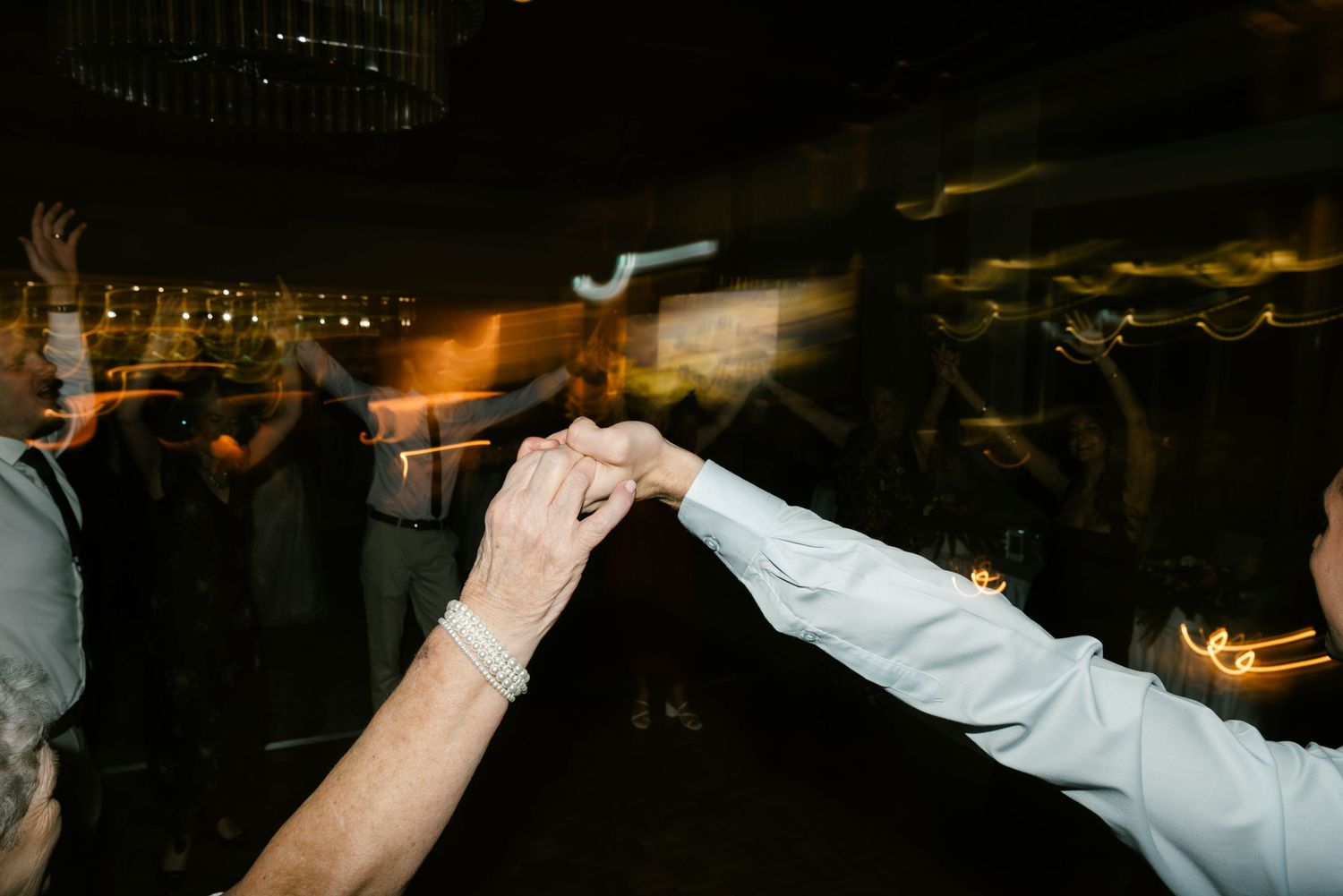 Two people holding hands while dancing at a nighttime event, captured with motion blur lighting.