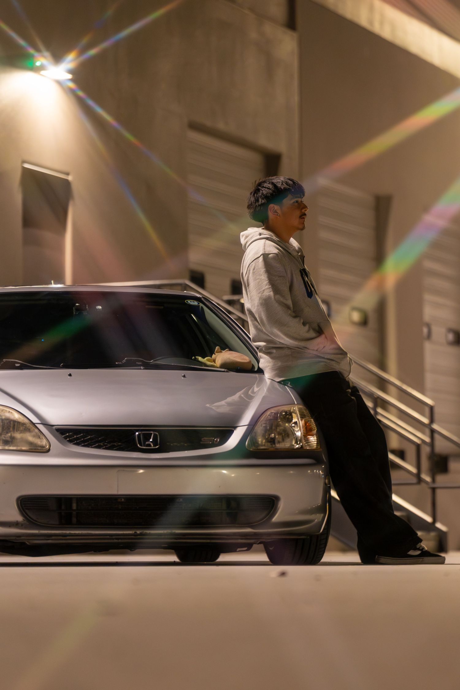 Person leaning against a silver Honda Civic at night in a parking garage with colorful lens flare effects.