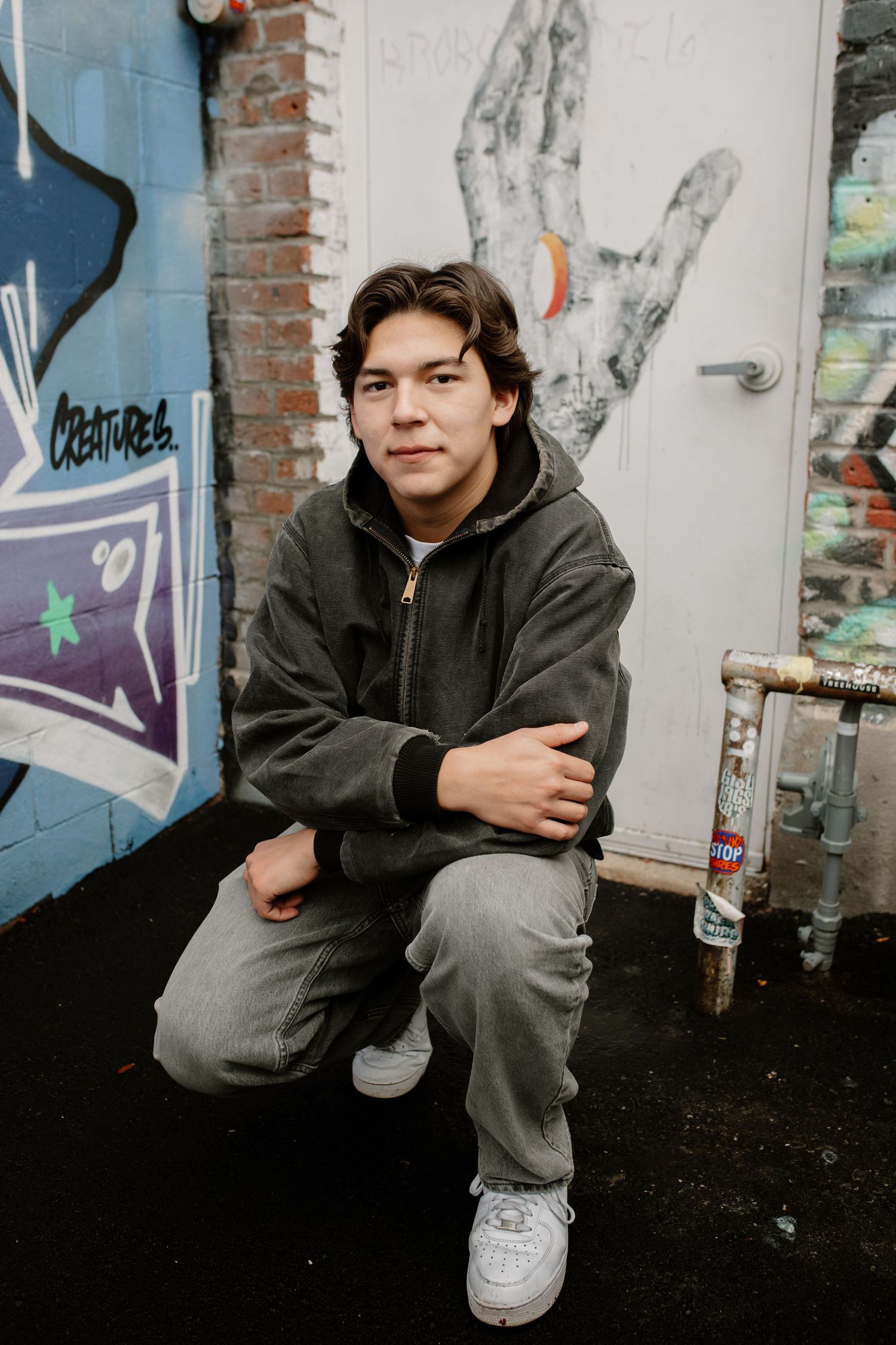 Urban photoshoot against graffiti wall wearing dark casual clothing.