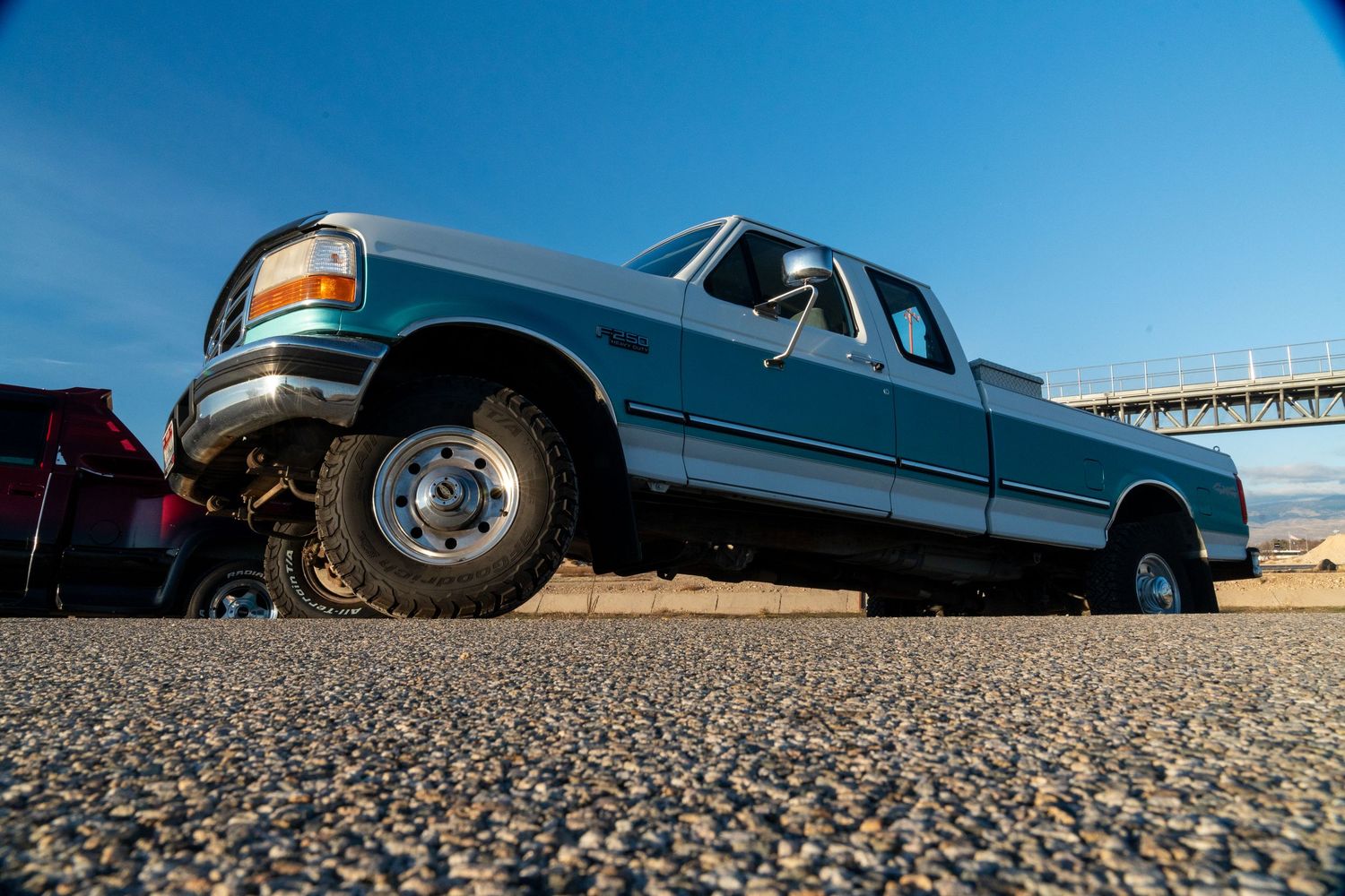 Low-angle view of vintage cars parked on gravel under blue sky.