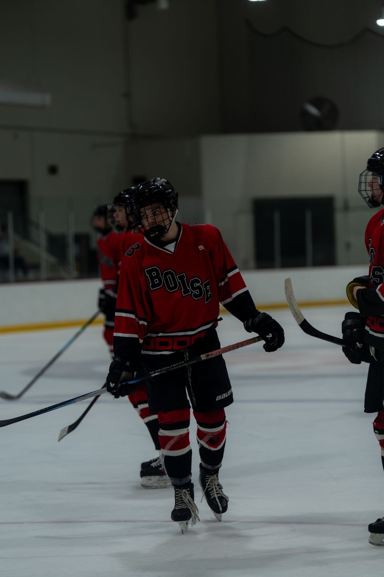 Hockey players in red jerseys skate on an indoor ice rink during a game or practice session.