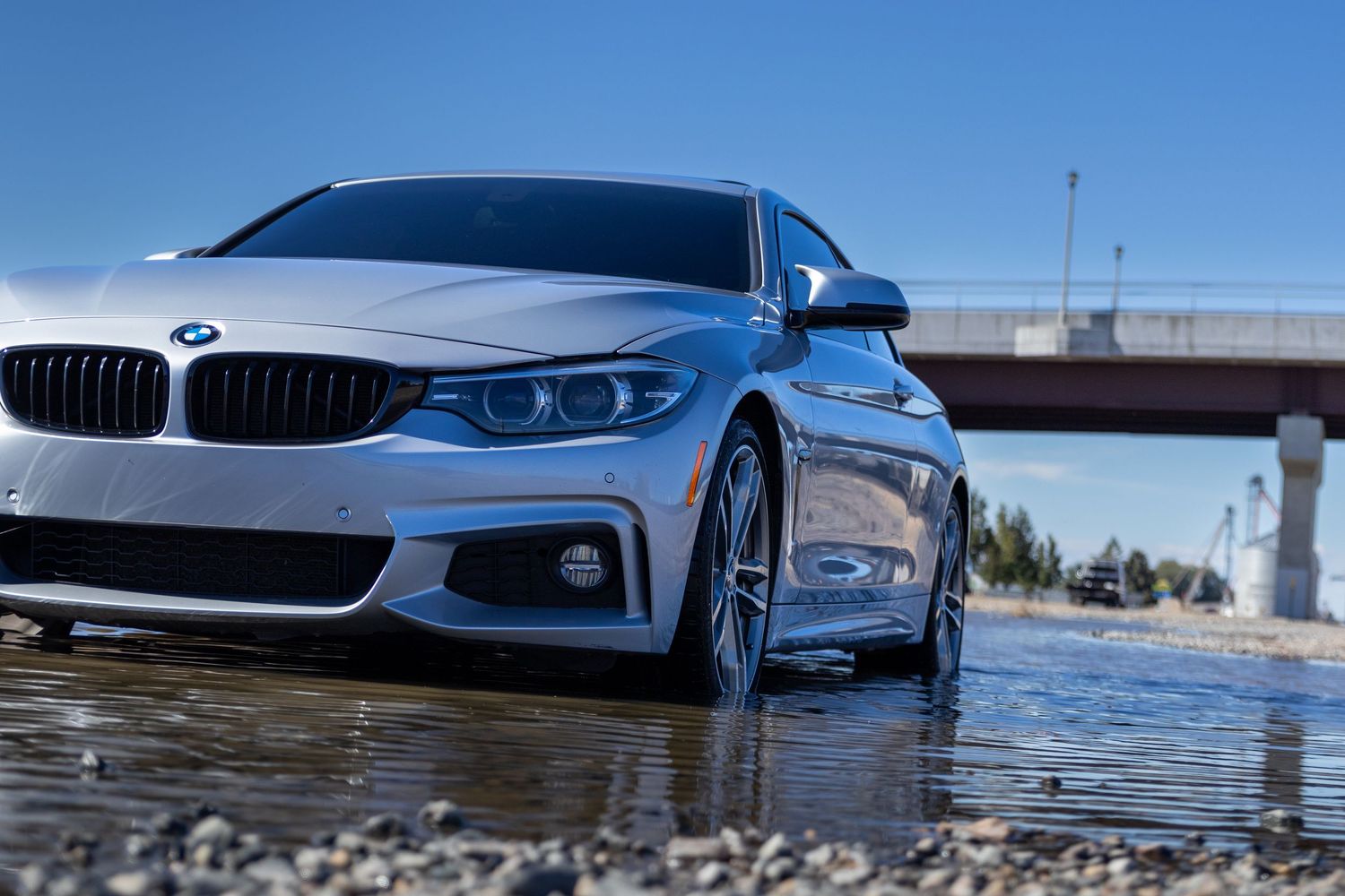 Luxury BMW and Audi vehicles photographed at water's edge with reflections.