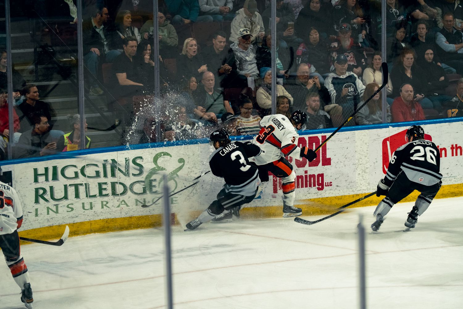 Ice hockey players collide near the boards during an intense game, with fans watching and a Higgins Rutledge Insurance ad visible.