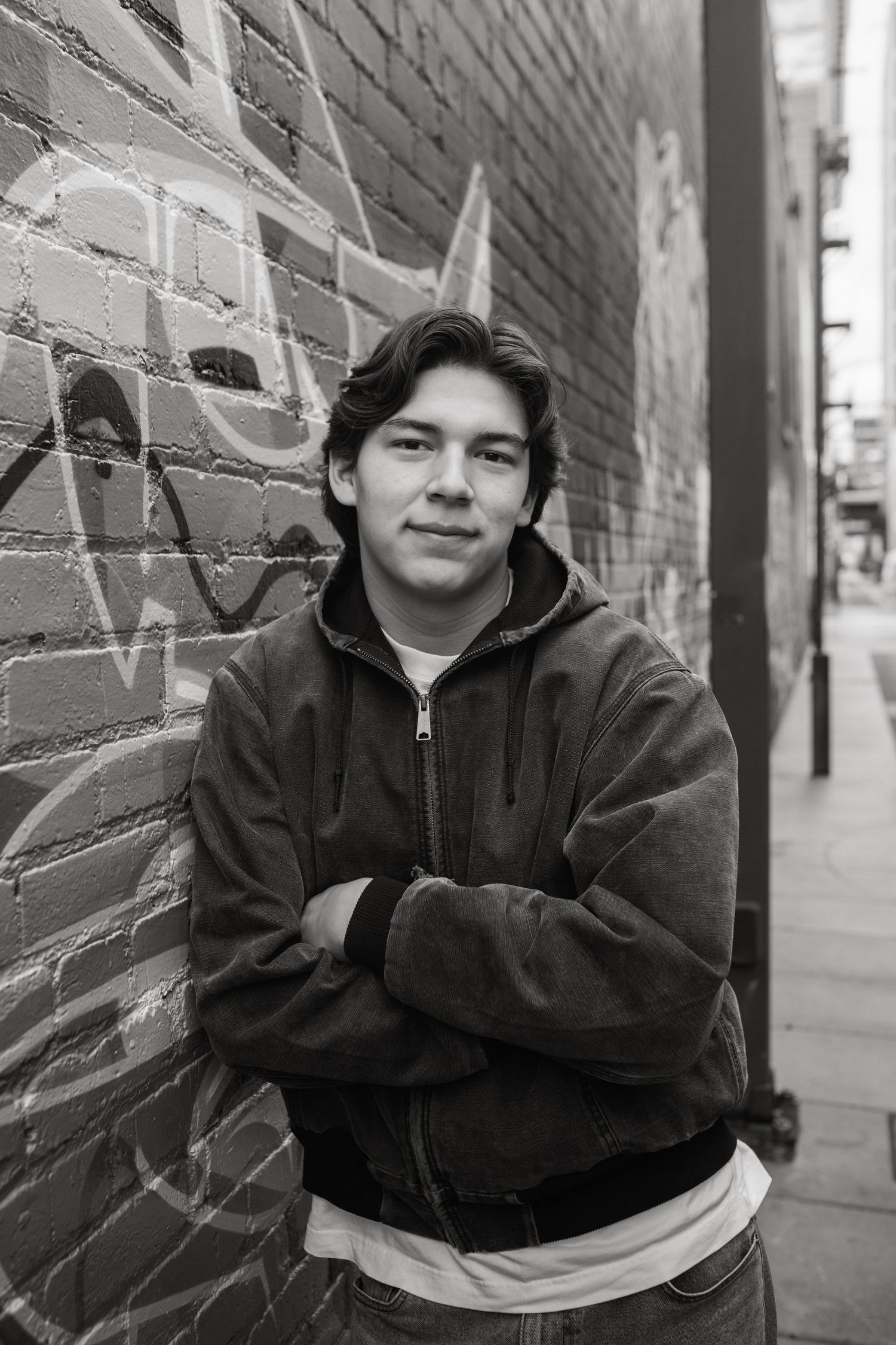 Black and white portrait against brick wall wearing dark jacket.