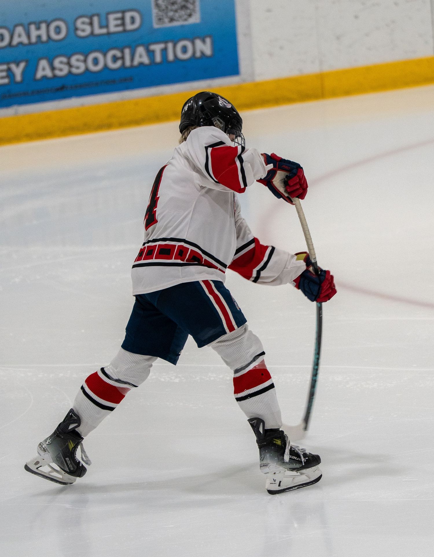 Hockey player in white and red uniform taking a shot on the ice.
