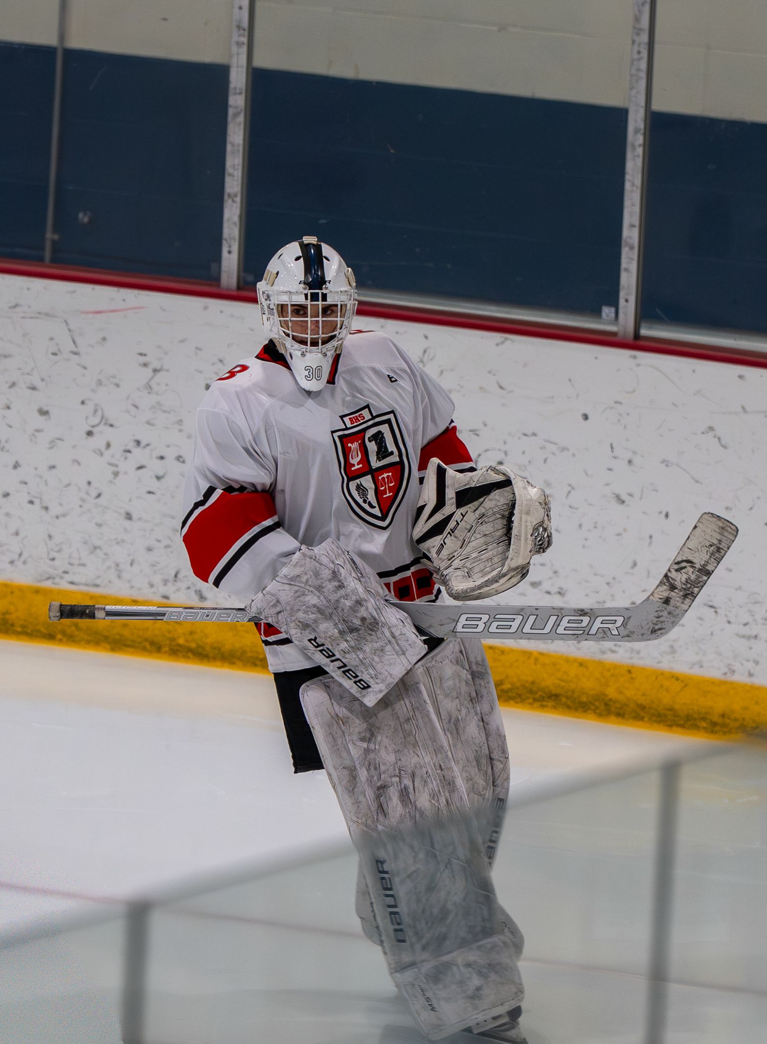Hockey goalie in white and red uniform with protective gear on ice rink.