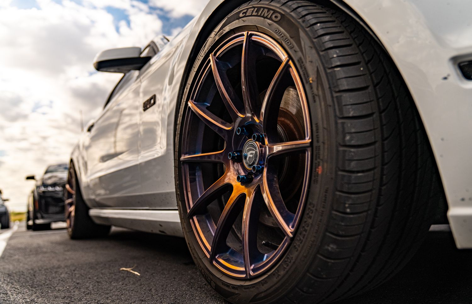 Close-up of a bronze multi-spoke alloy wheel on a white sports car parked on a road.