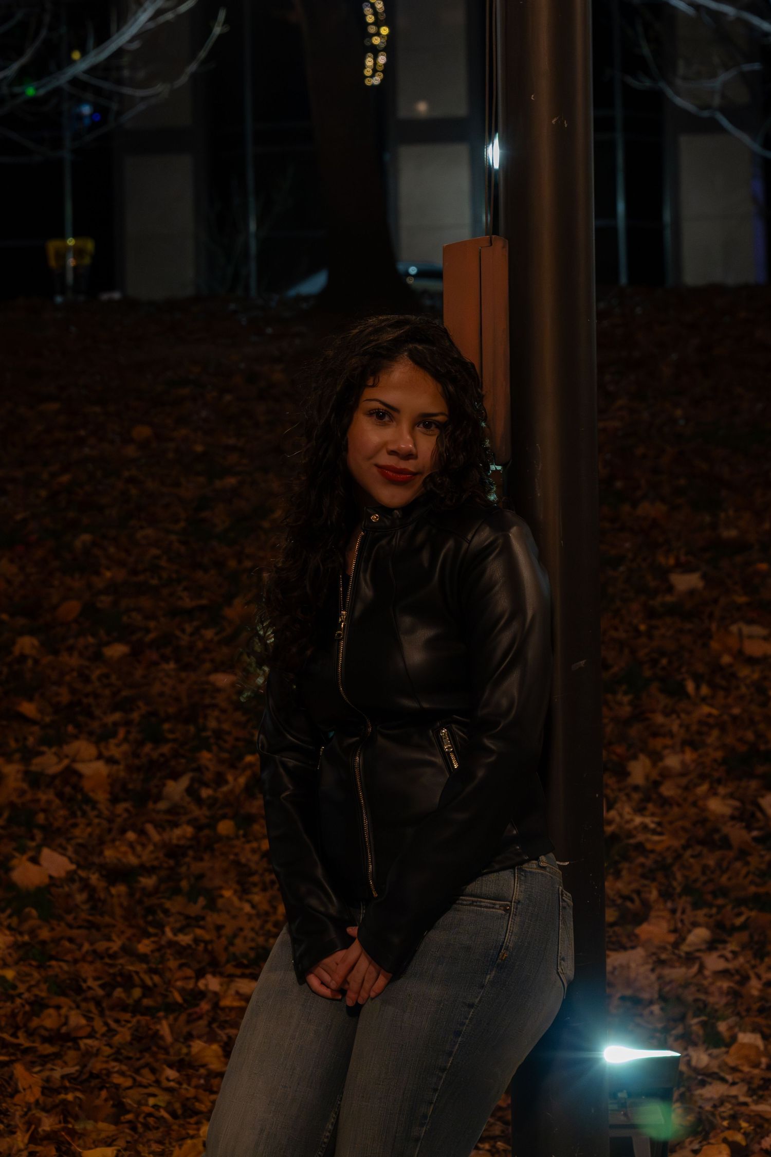 Autumn night scene with fallen leaves illuminated by street lights.