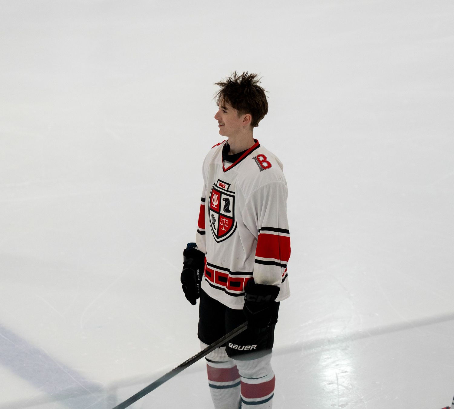 Hockey player in white uniform with red accents standing on ice.