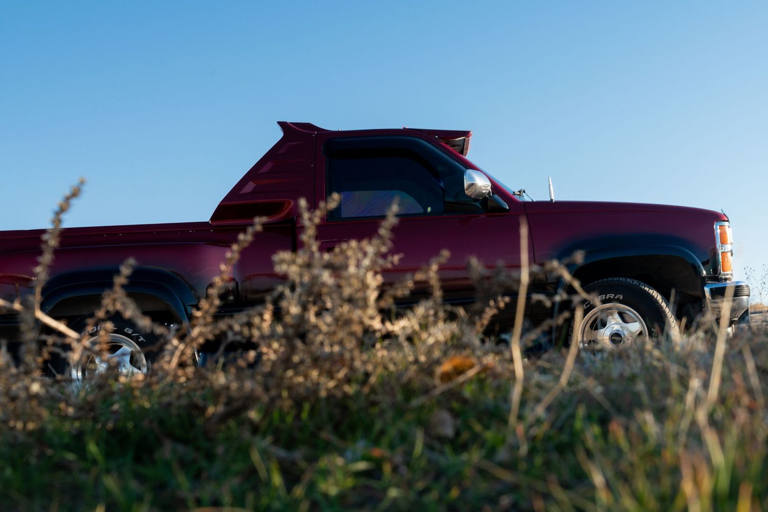 Classic cars lined up against a sunset sky with dramatic silhouettes.