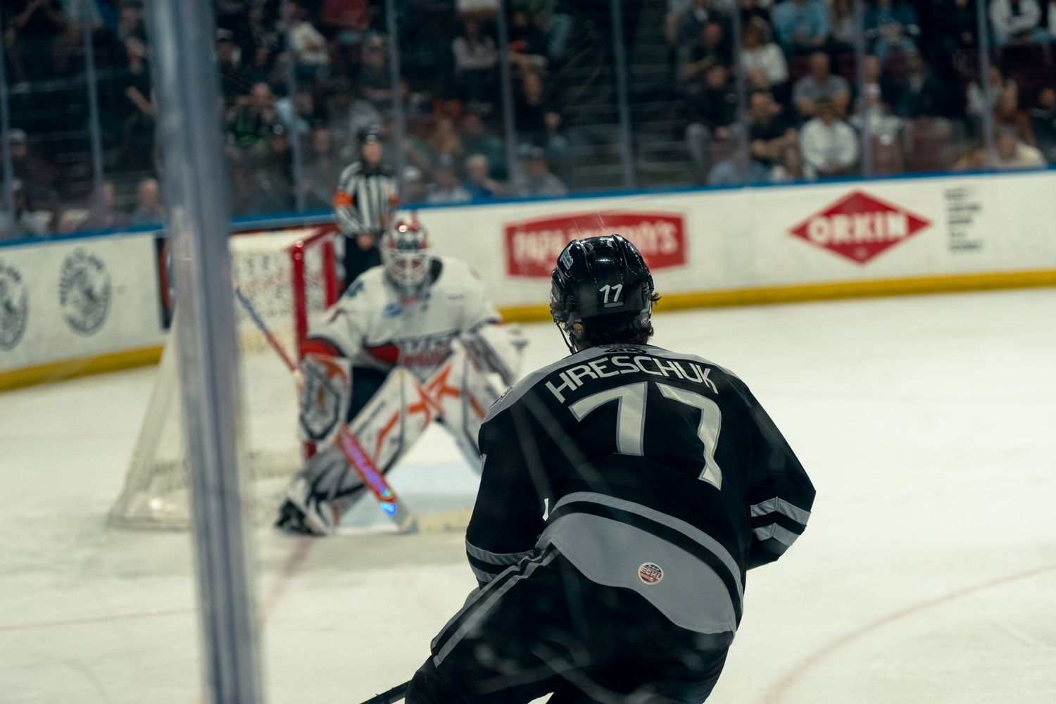 Hockey player #77 Hrechuk skating toward goalie during an indoor ice hockey game.