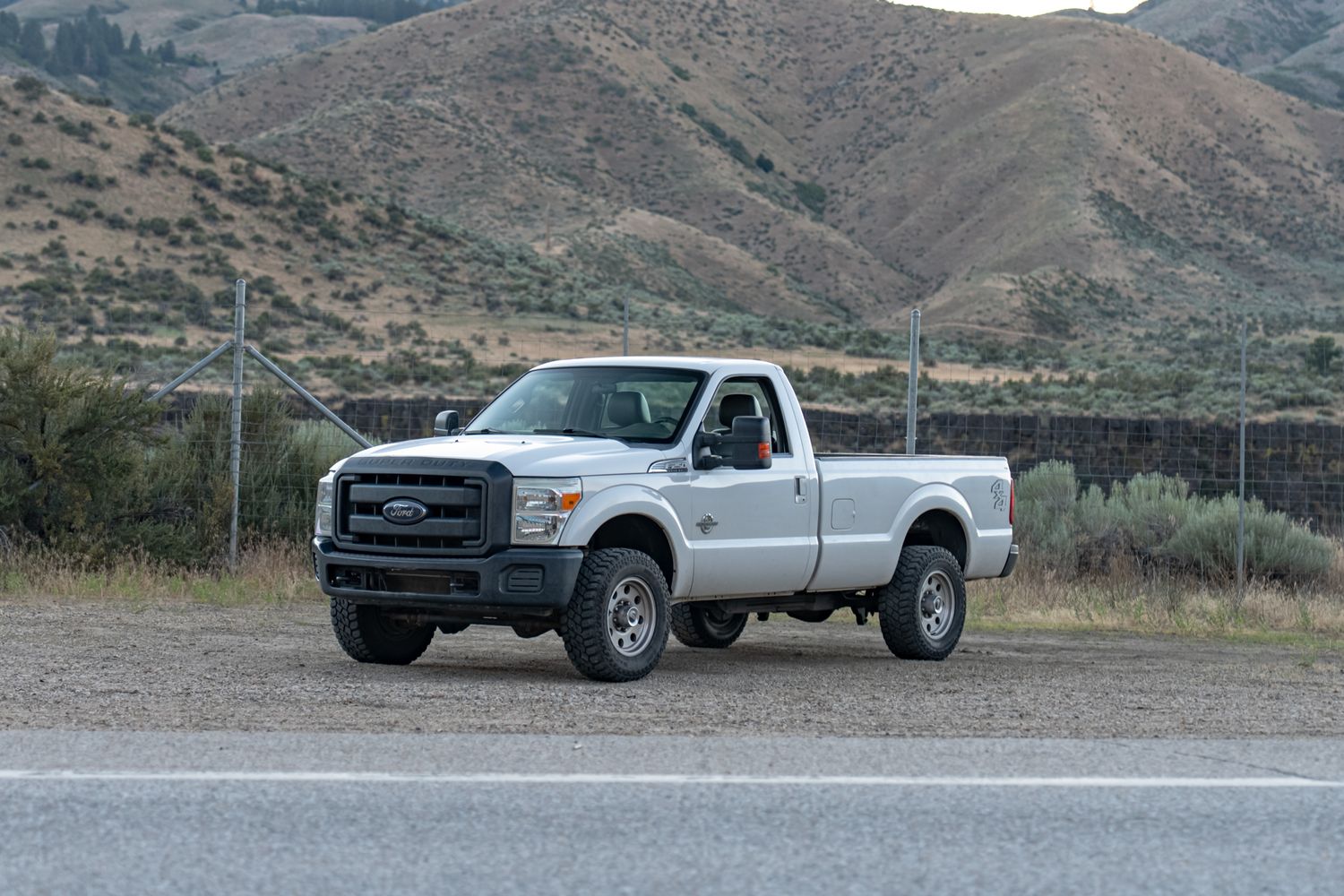White Ford F-250 pickup truck parked on a road with desert hills and mountains in the background.