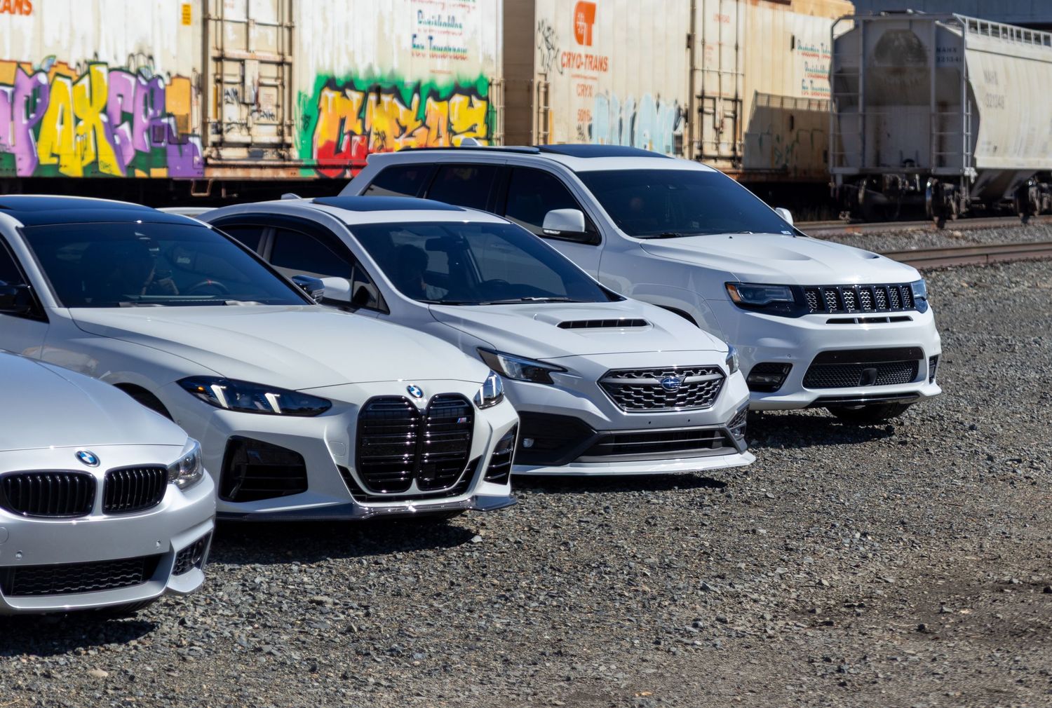 Row of modern luxury cars parked against graffiti-covered wall.
