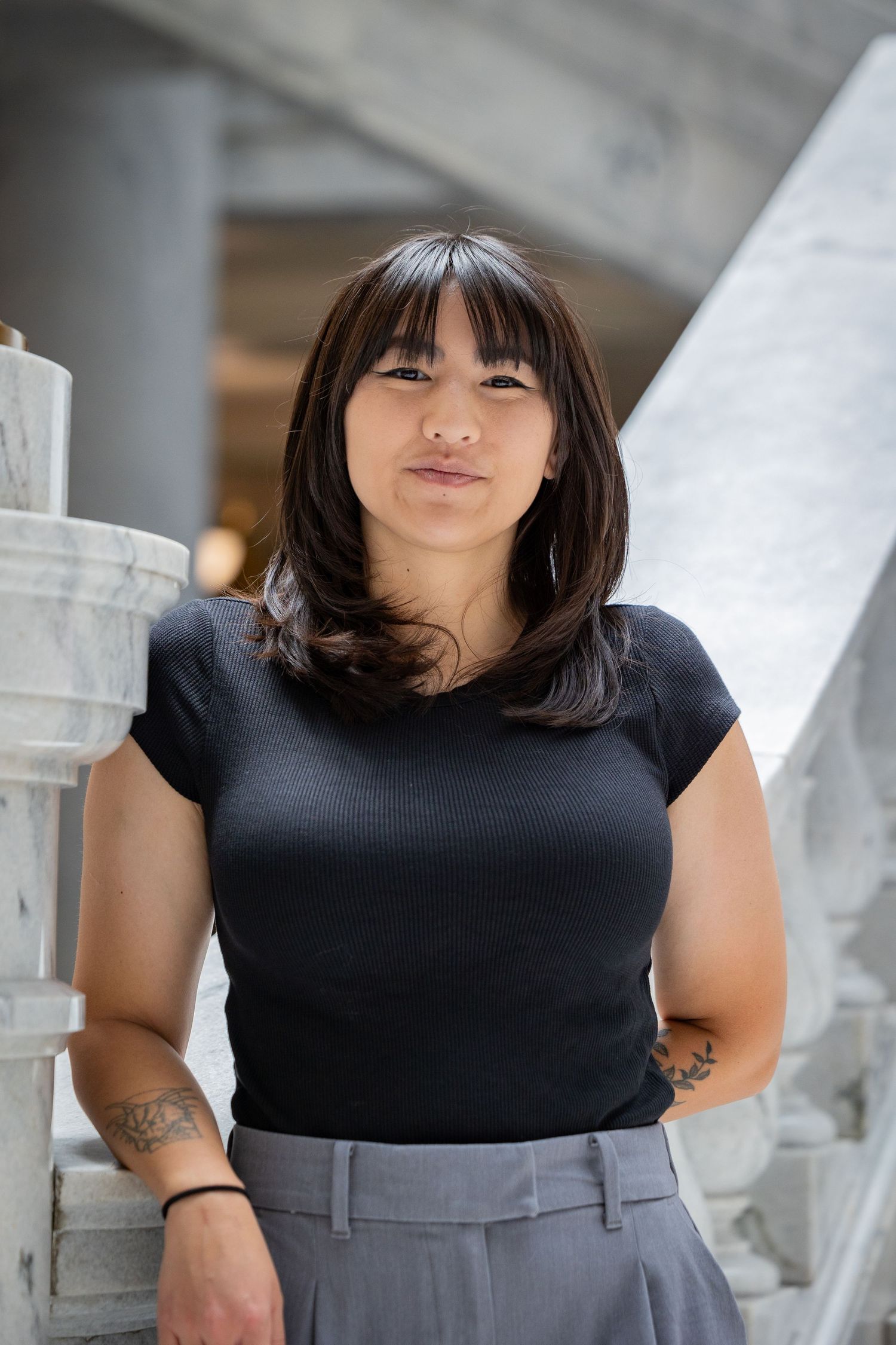 Professional portrait of person in black shirt and gray pants against marble building.