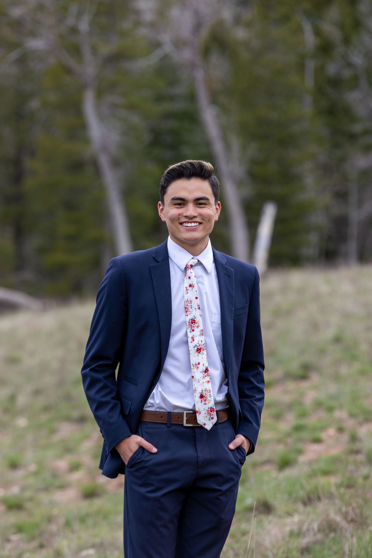 Formal business portraits in navy suit against natural forest background.