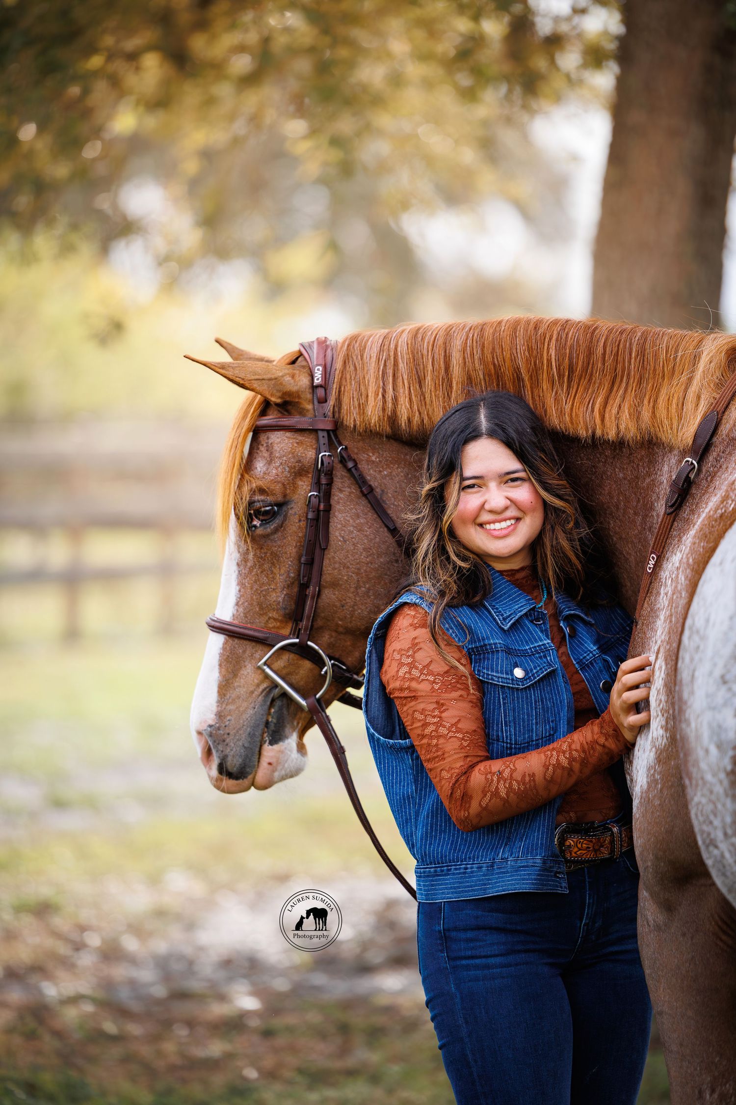 Brown horse with flowing mane stands next to someone in denim overalls and brown jacket.