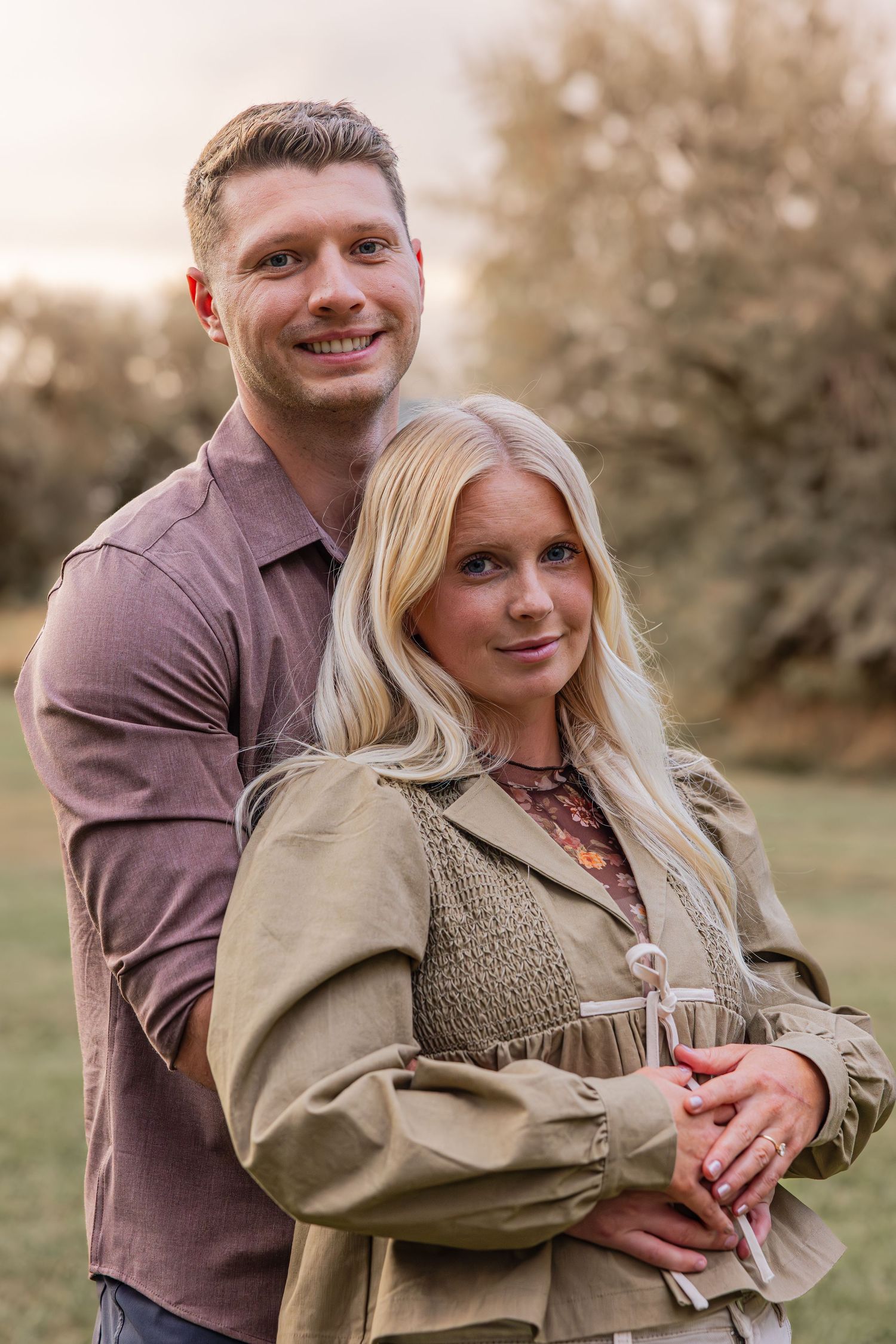 A couple poses together outdoors during golden hour for a portrait.
