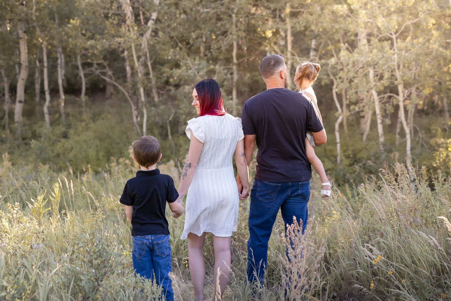 Family walking together through tall grass field at sunset.