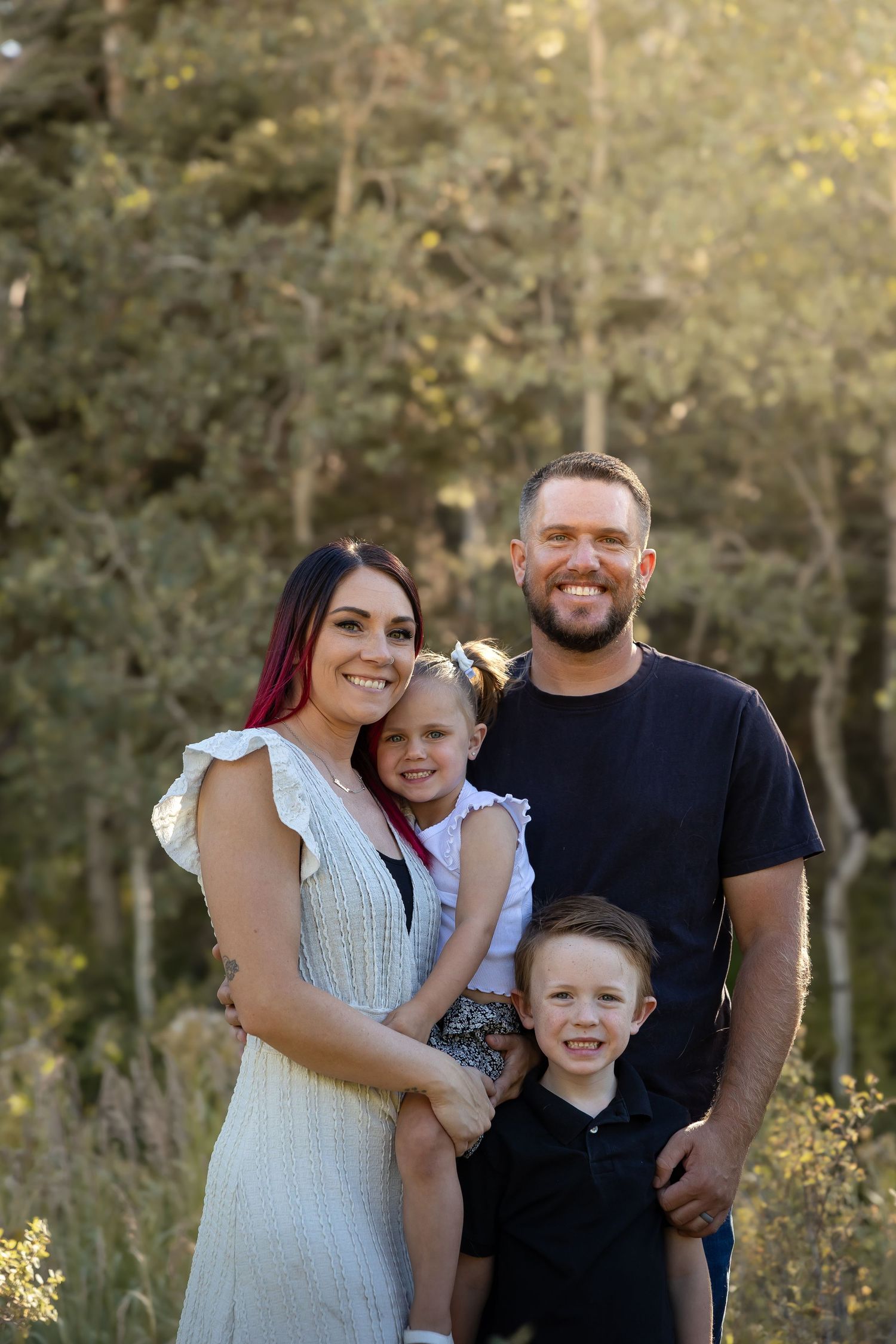 Family portrait in casual attire against wooded background during golden hour.