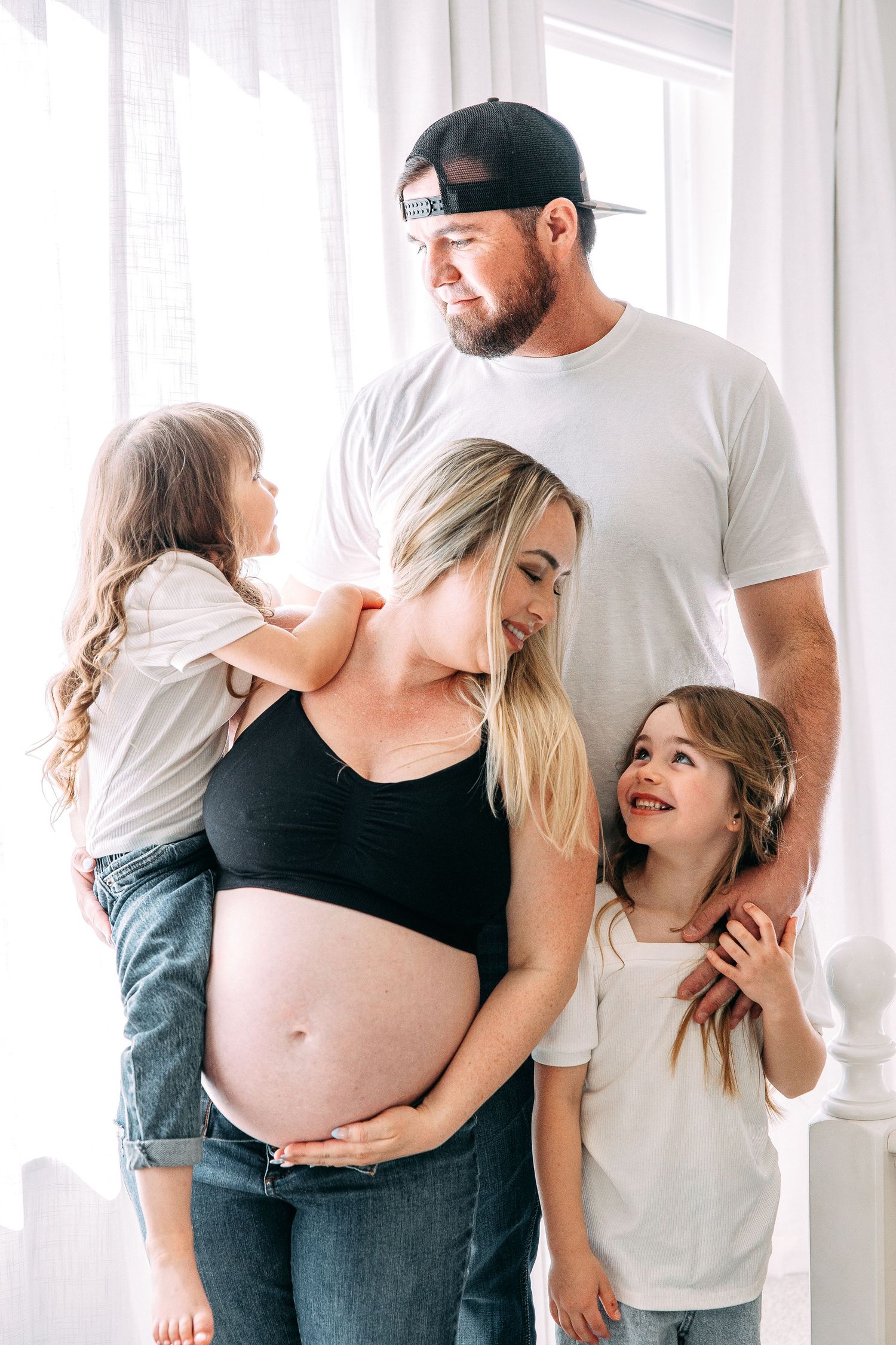An expectant couple shares tender moments in a bright indoor photoshoot.