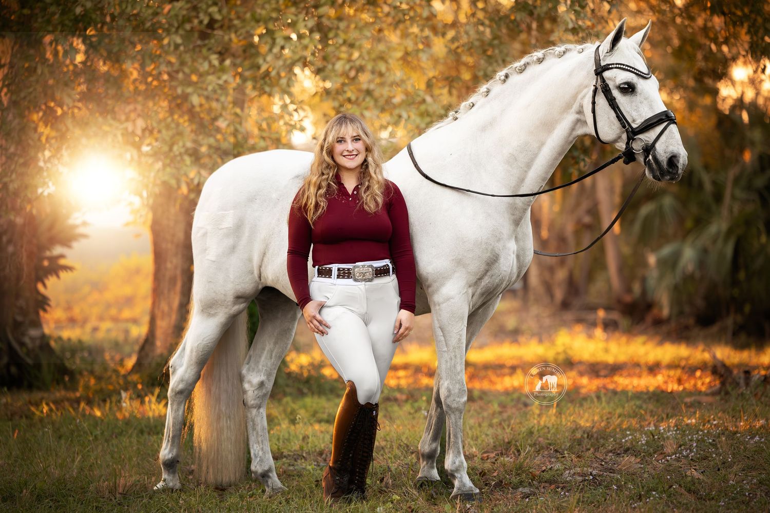 A beautiful white horse and rider pose in an autumn setting with golden sunlight filtering through trees.