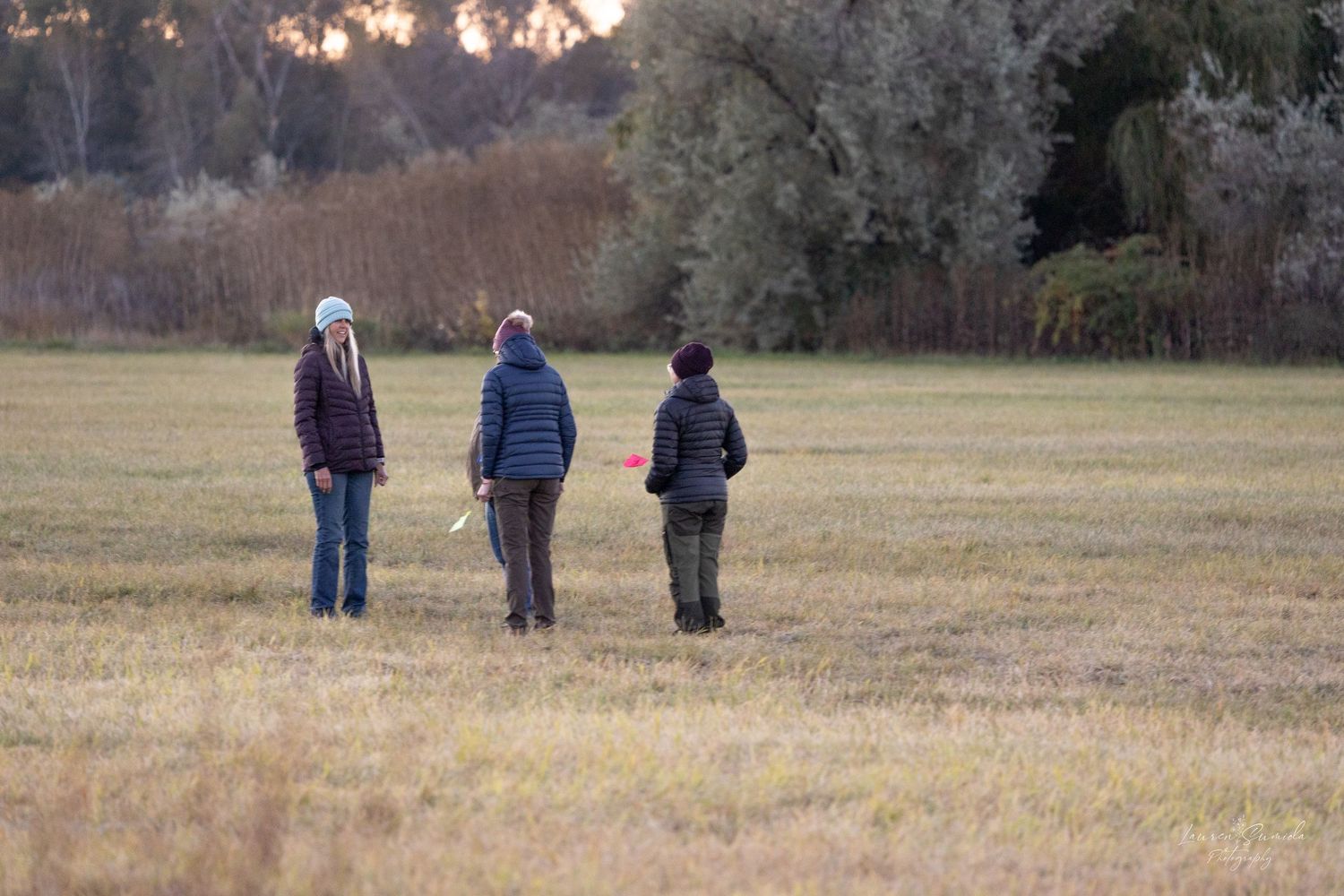 Three people walking across an open field at sunset.