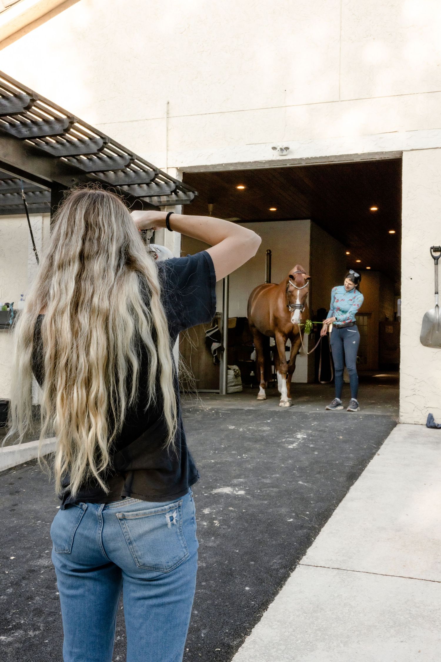 Photographer with long blonde hair taking pictures of horse in stable doorway.