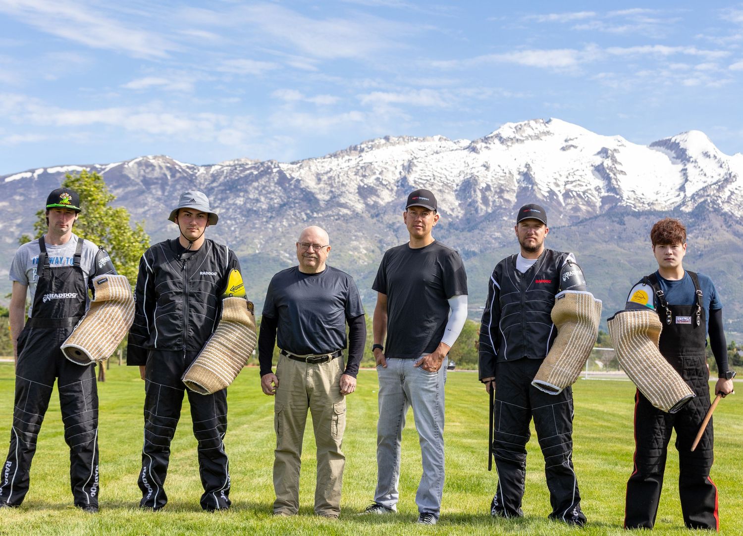 Police K9 training team poses with training equipment against snowy mountain backdrop.