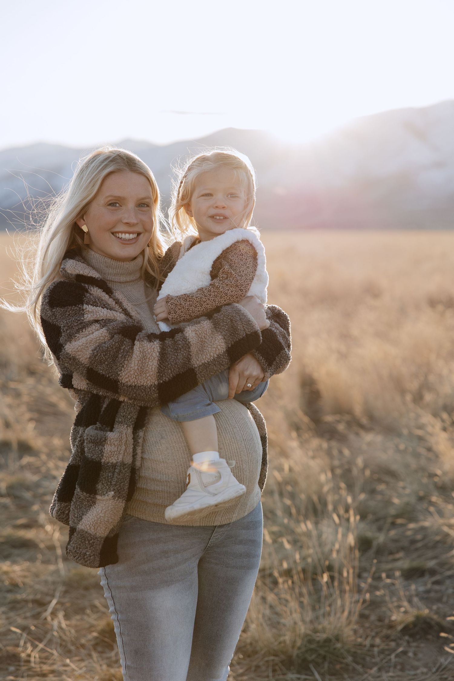 Mother and child share playful moments in a sunlit field during golden hour.