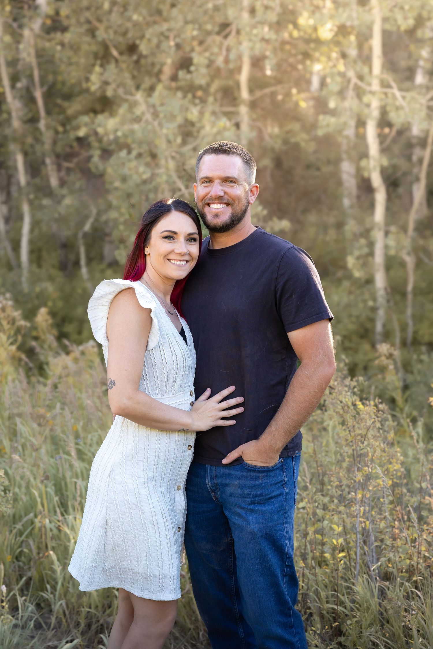 Couple embracing and laughing in white and dark outfits among wild grasses.